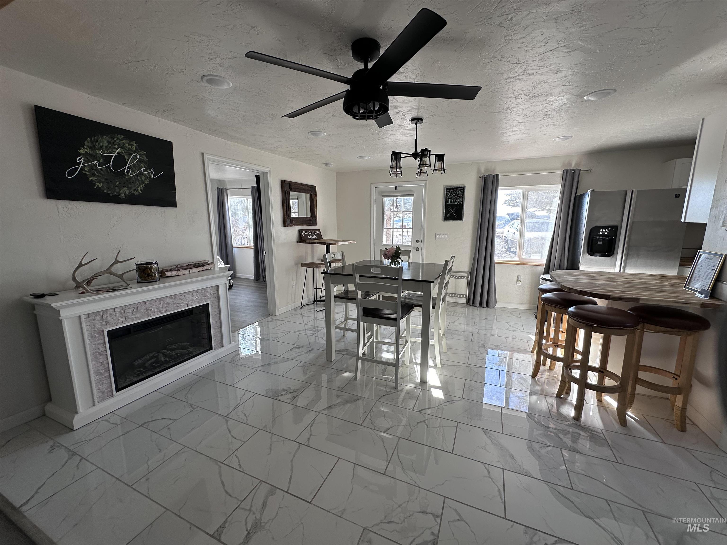 Dining space featuring light marble finish floors, a textured ceiling, a glass covered fireplace, and ceiling fan