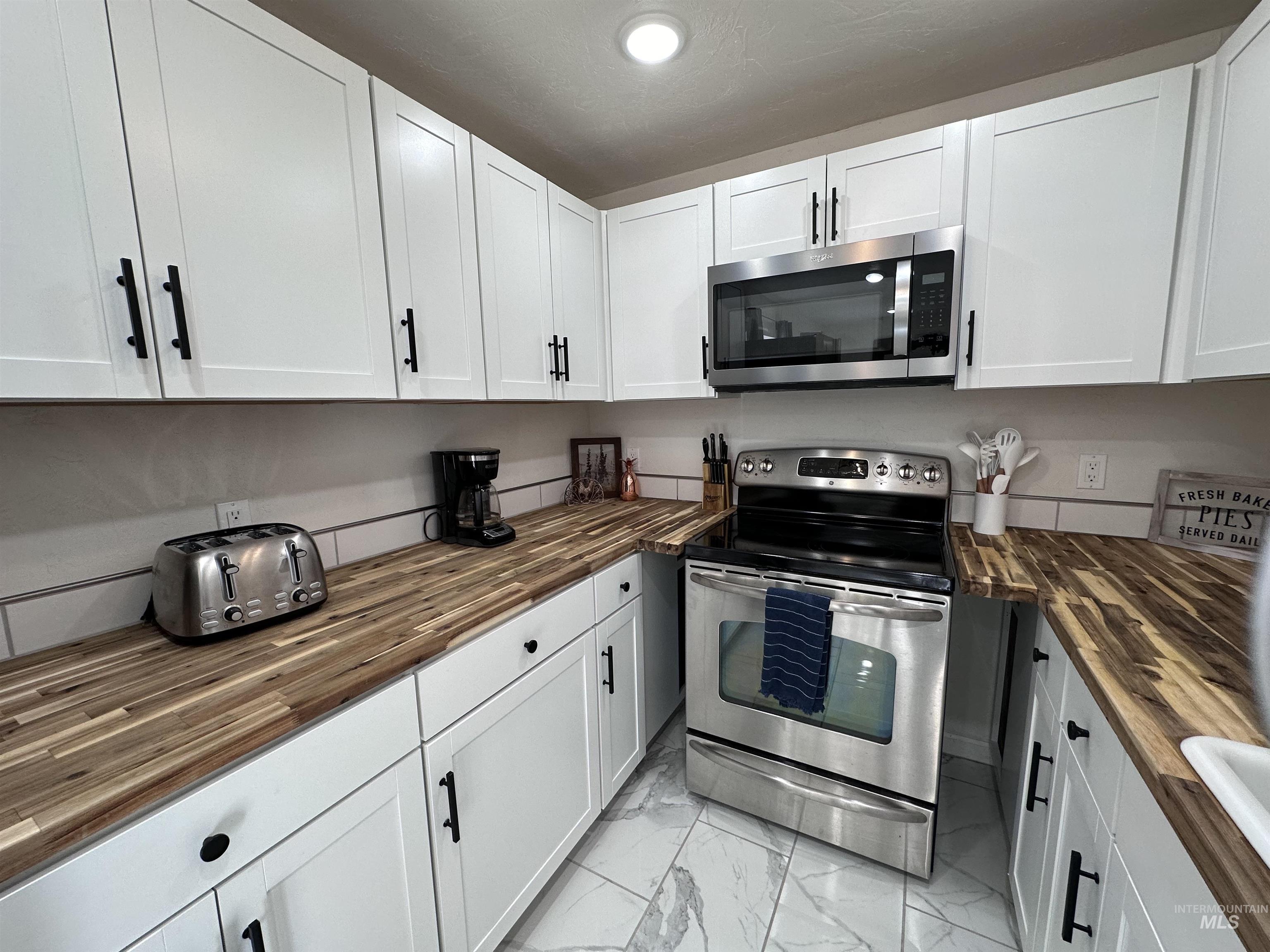 Kitchen with wood counters, appliances with stainless steel finishes, and white cabinets