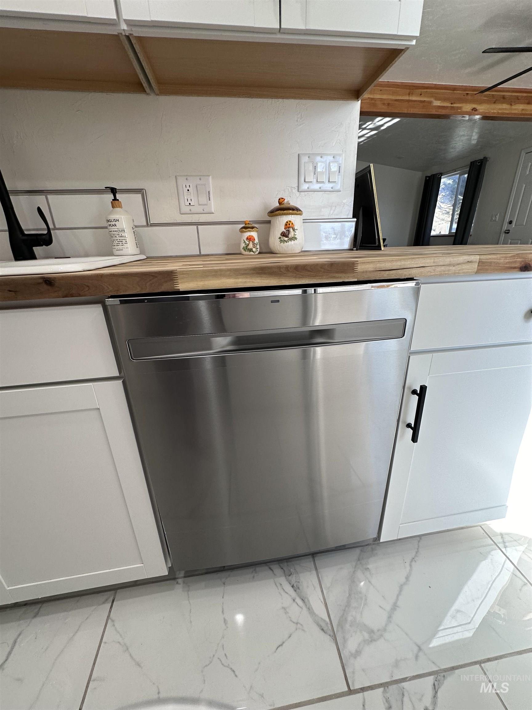 Kitchen view of dishwasher, white cabinetry, and wooden counters