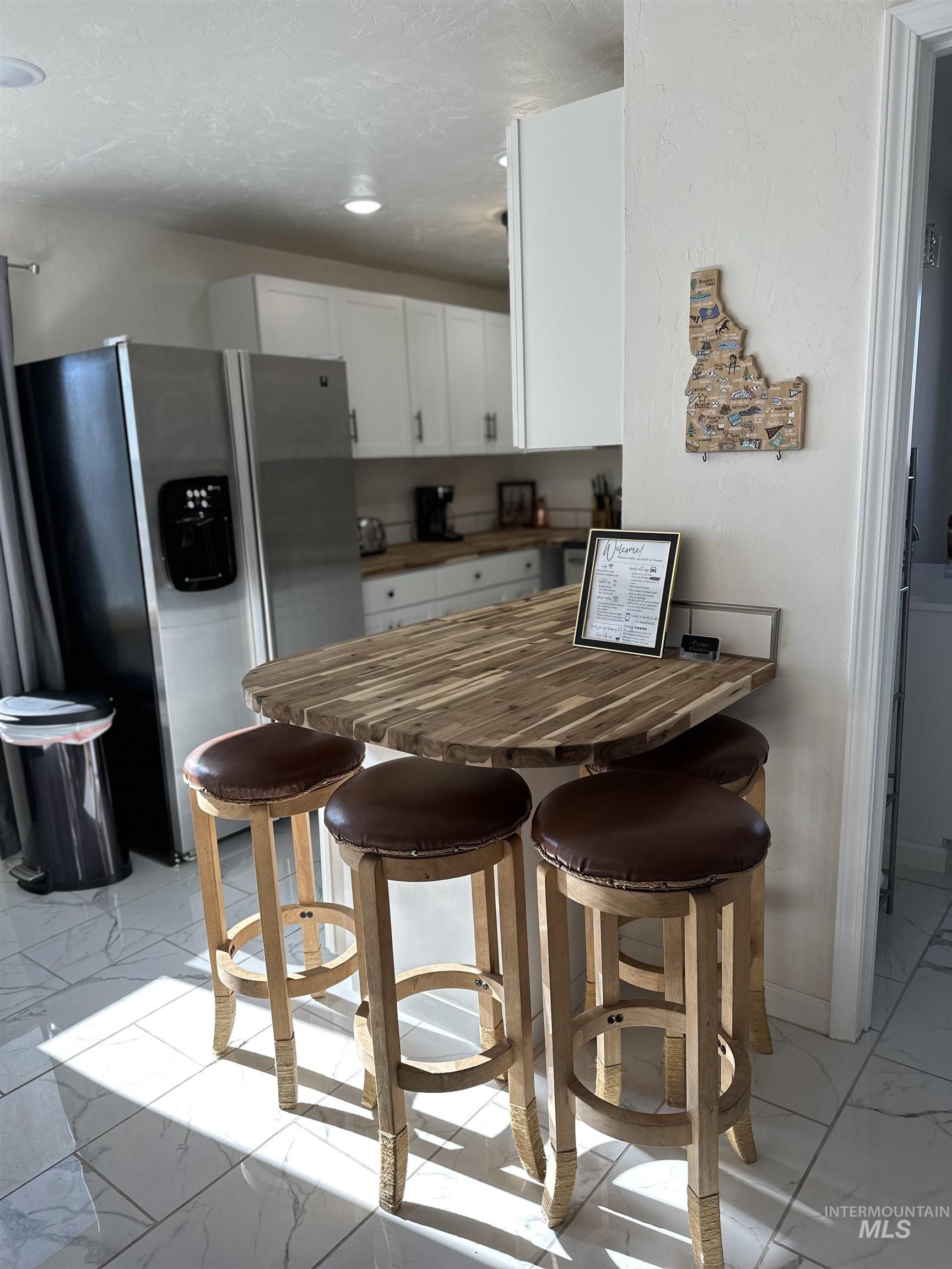 Kitchen featuring light marble finish flooring, a breakfast bar, wooden counters, stainless steel fridge, and a peninsula