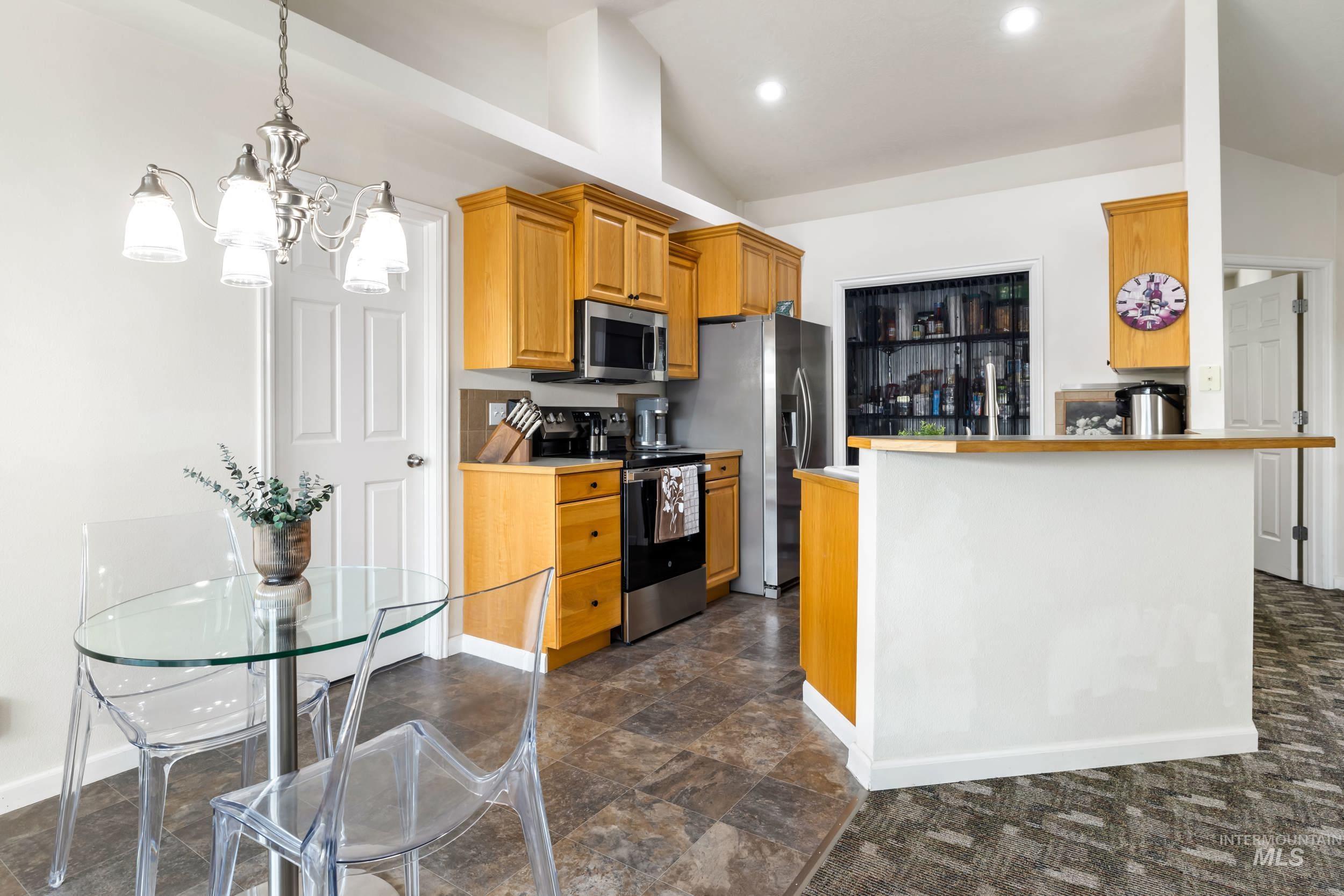 Kitchen with stainless steel appliances, hanging light fixtures, light countertops, a chandelier, and brown cabinets