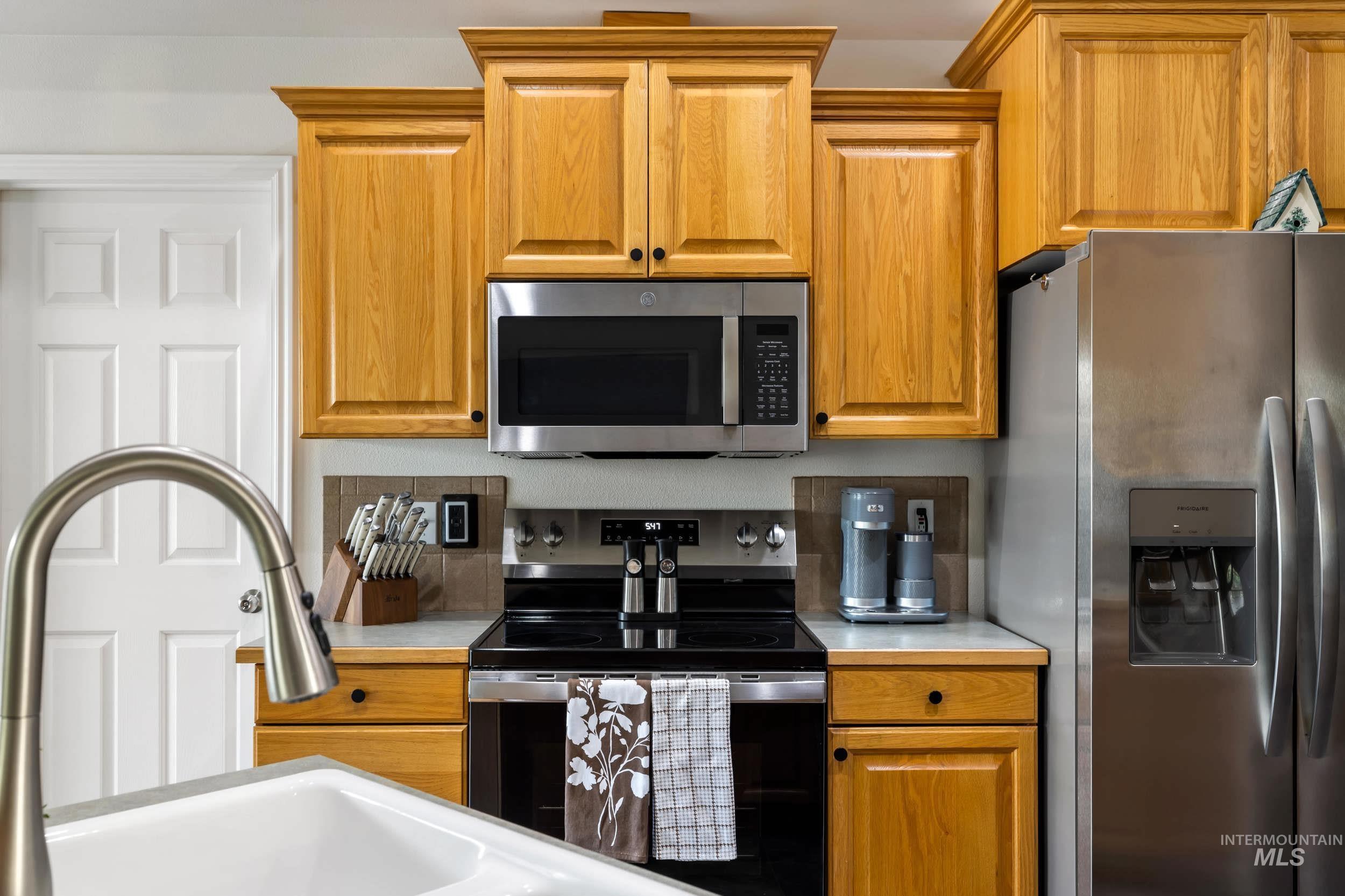 Kitchen with appliances with stainless steel finishes, light countertops, brown cabinets, and decorative backsplash