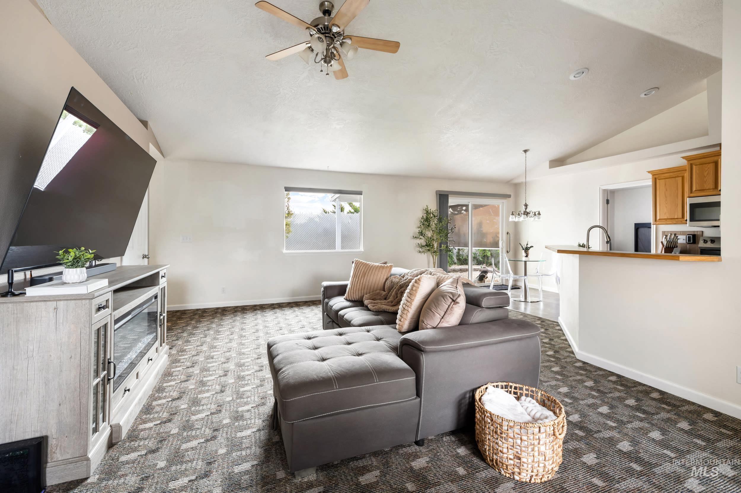 Living area with vaulted ceiling, a chandelier, dark carpet, and ceiling fan