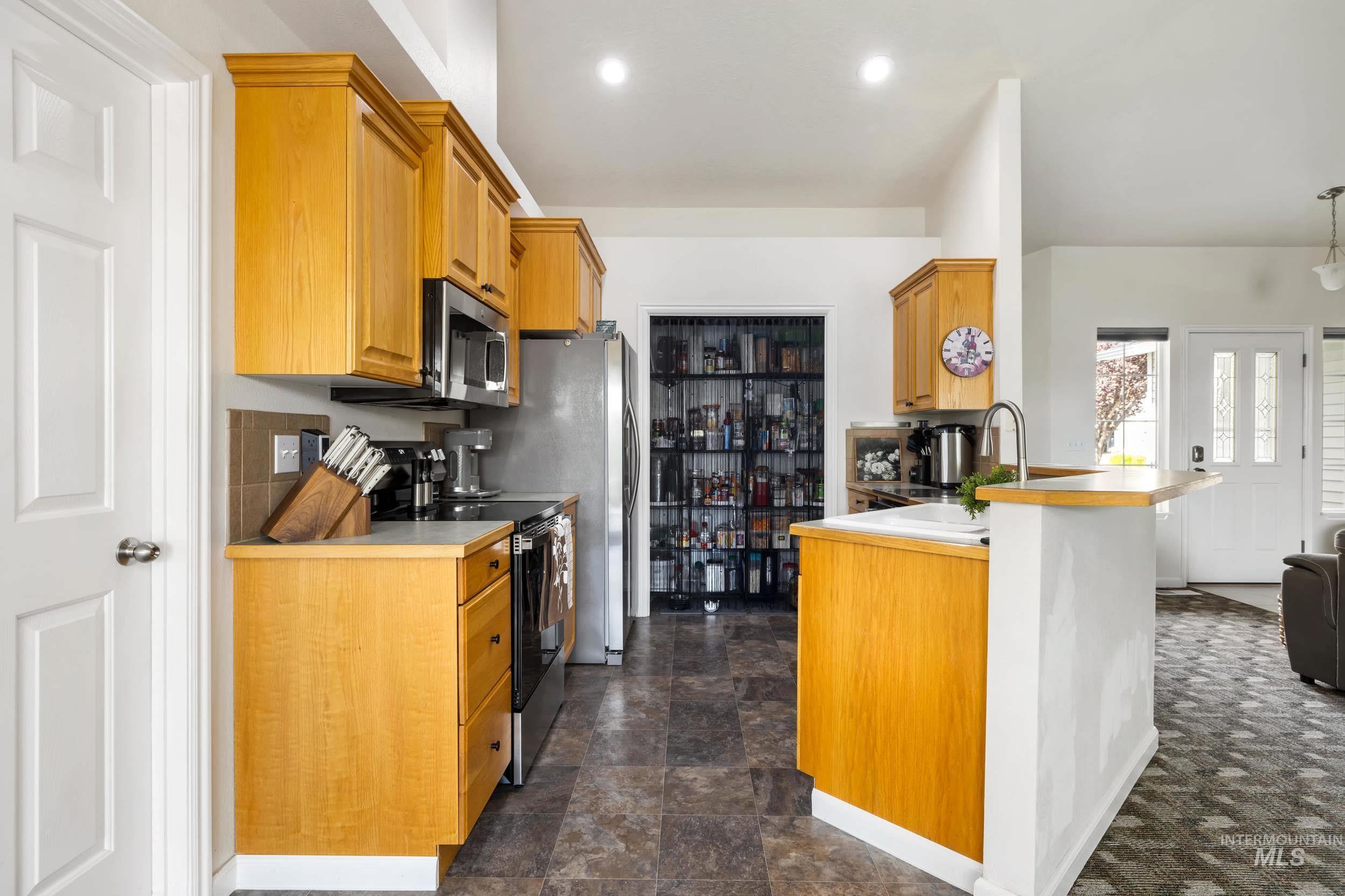 Kitchen with electric range, a peninsula, brown cabinetry, light countertops, and stainless steel microwave