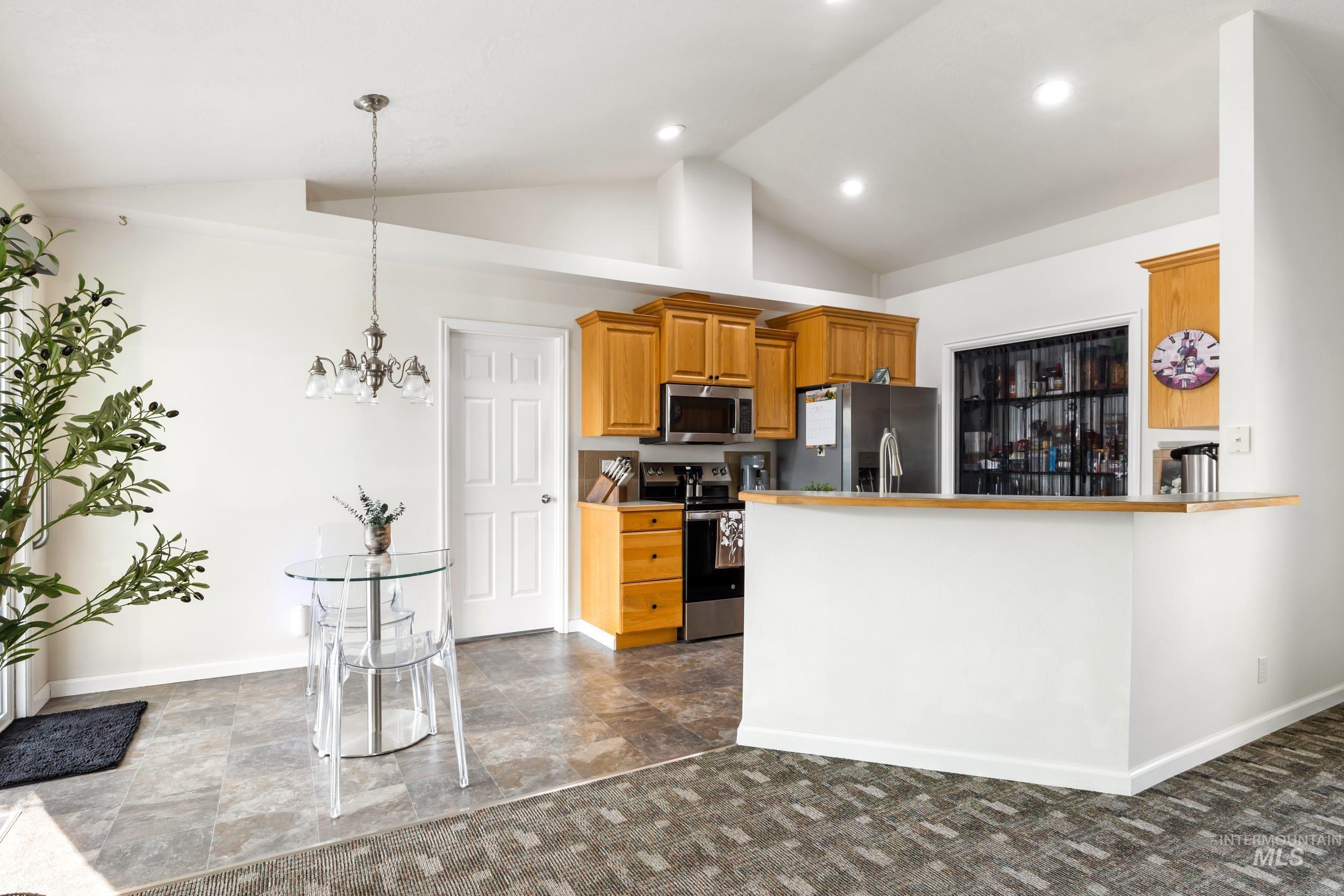 Kitchen with stainless steel appliances, brown cabinetry, pendant lighting, light countertops, and a peninsula