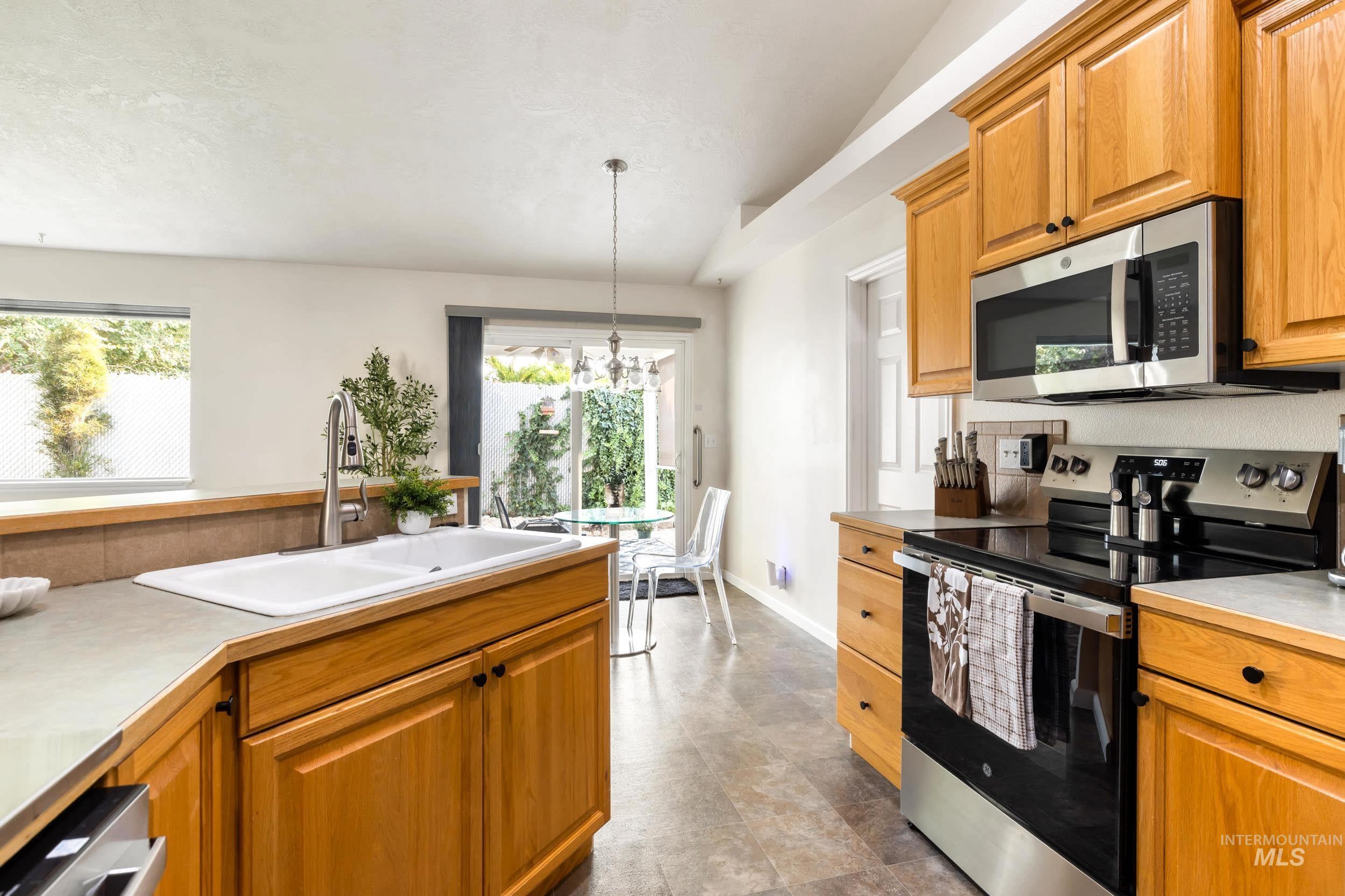 Kitchen with appliances with stainless steel finishes, pendant lighting, a chandelier, light countertops, and brown cabinetry
