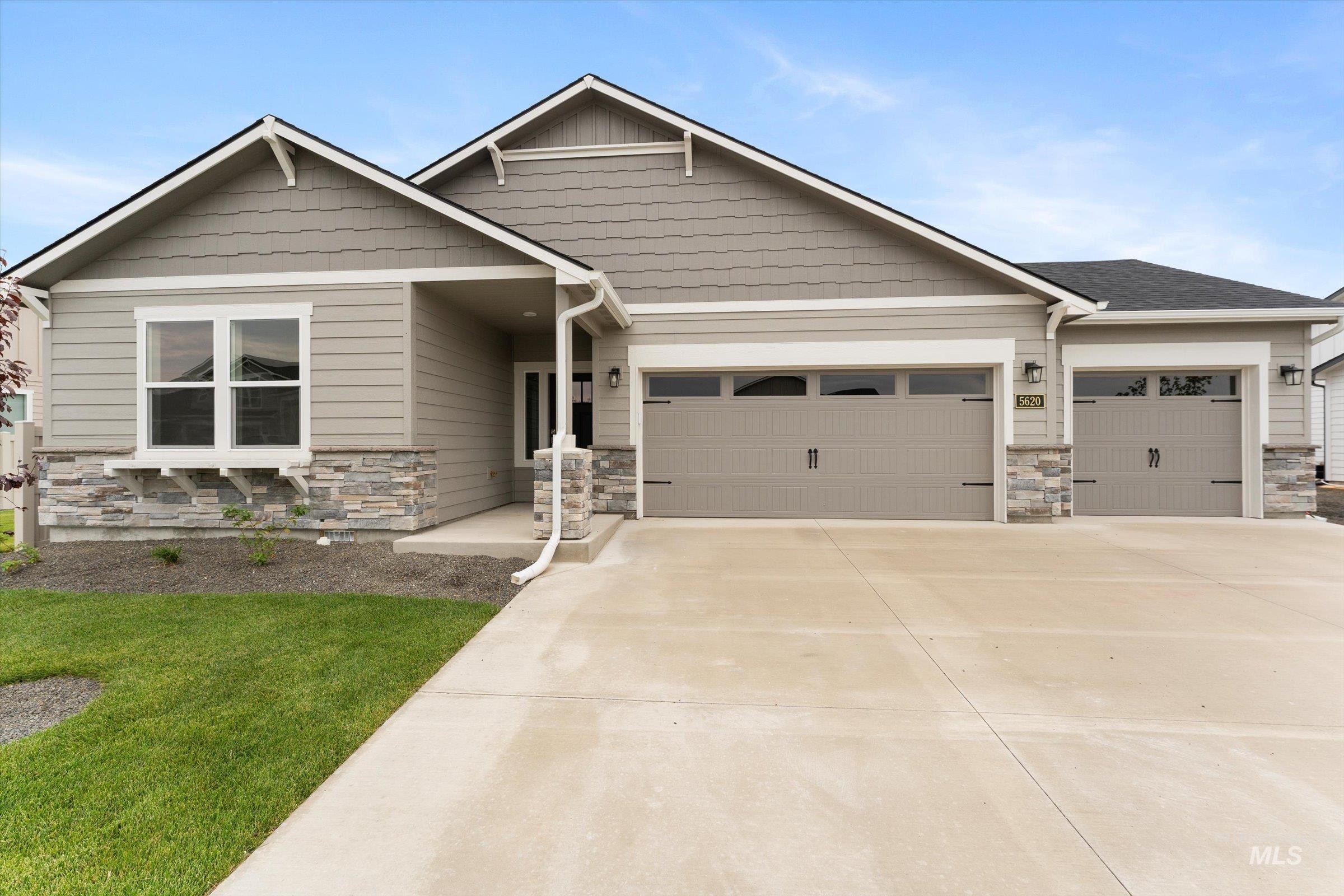 Craftsman house featuring stone siding, a garage, driveway, and a front lawn