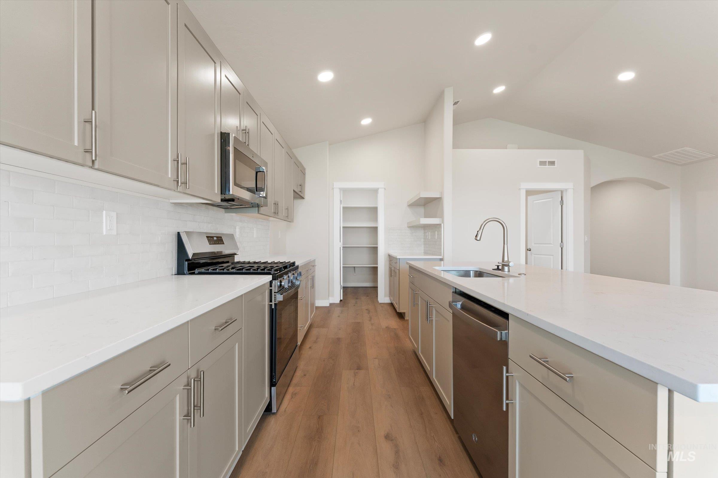 Kitchen featuring decorative backsplash, appliances with stainless steel finishes, an island with sink, light wood-style flooring, and light stone countertops