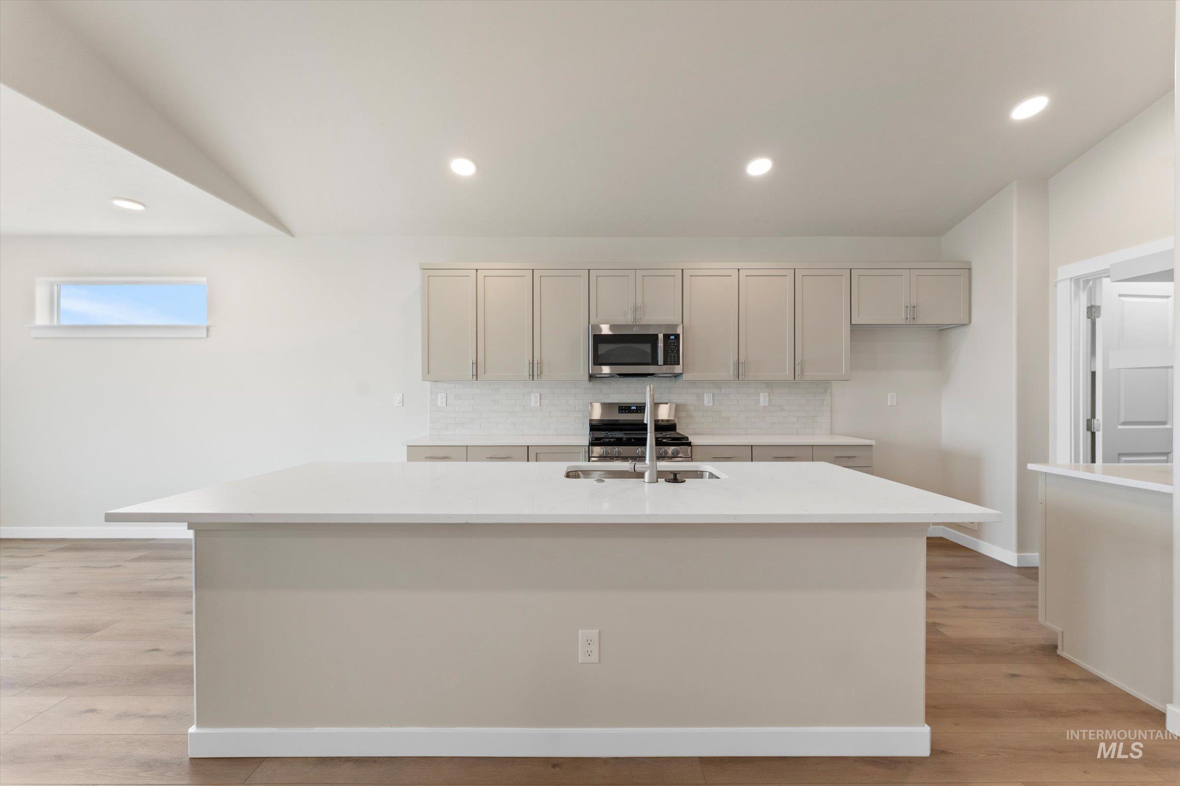 Kitchen with recessed lighting, decorative backsplash, an island with sink, stainless steel appliances, and light stone countertops