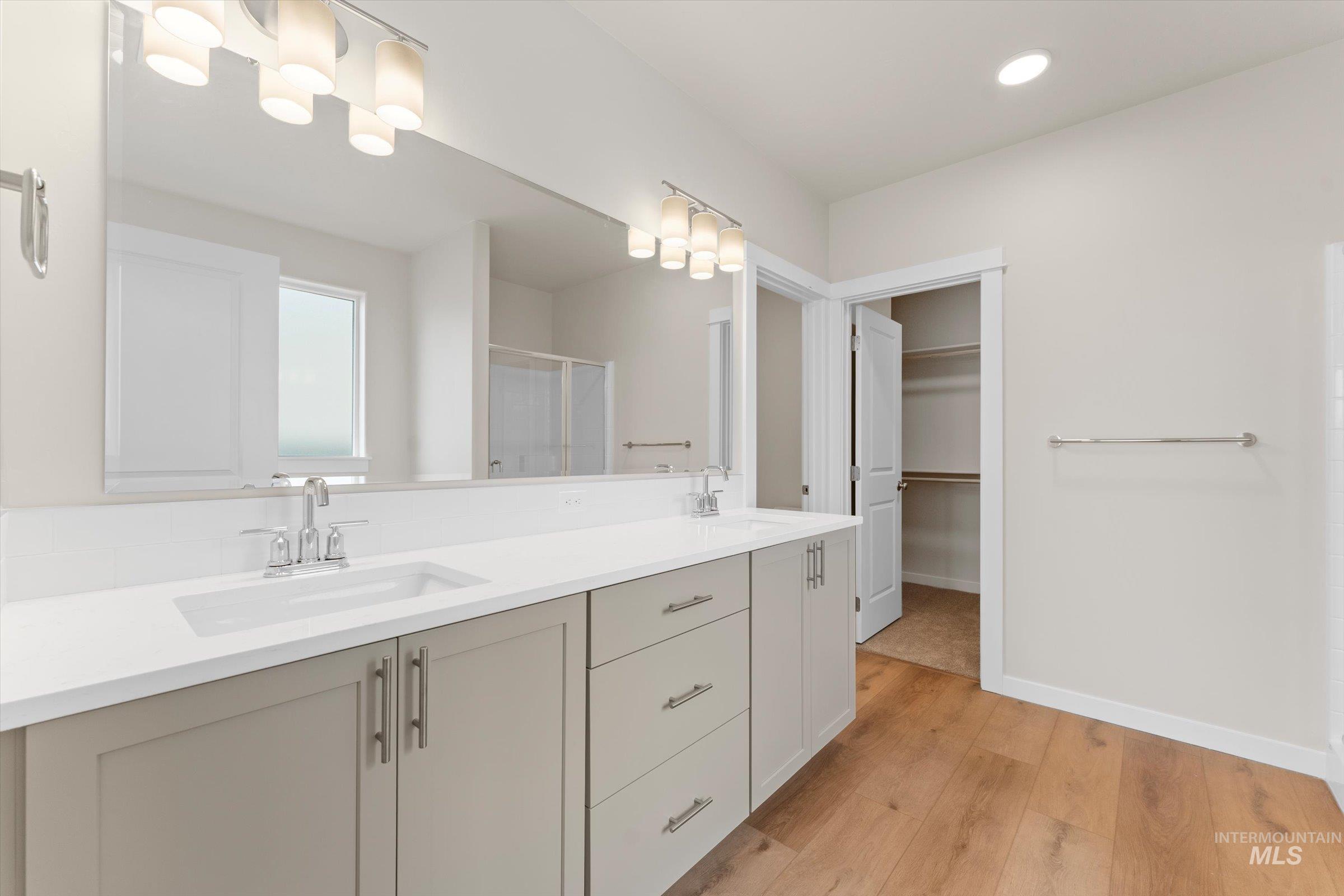 Full bathroom featuring a shower stall, light wood finished floors, double vanity, a spacious closet, and recessed lighting