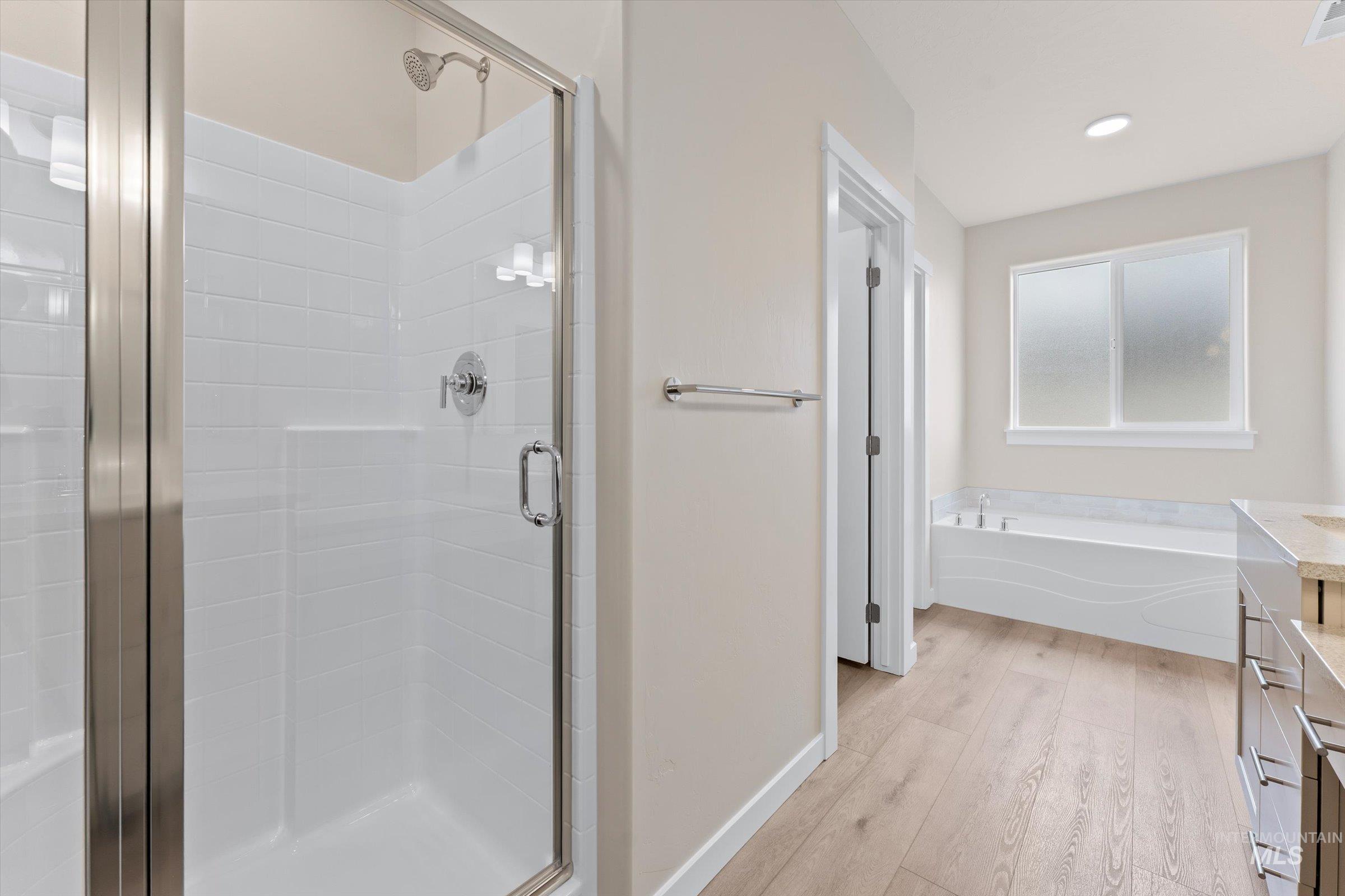 Bathroom featuring vanity, a stall shower, light wood-style floors, and a garden tub