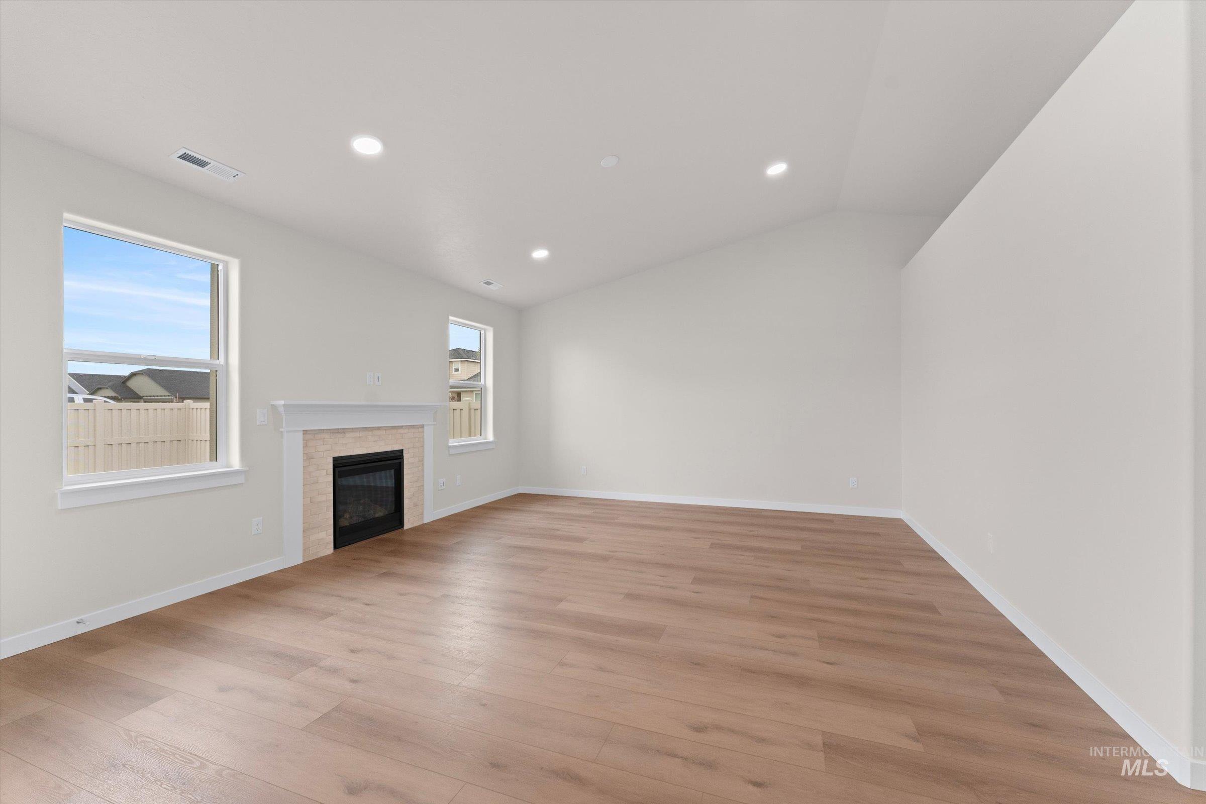 Unfurnished living room with a glass covered fireplace, recessed lighting, light wood finished floors, and lofted ceiling
