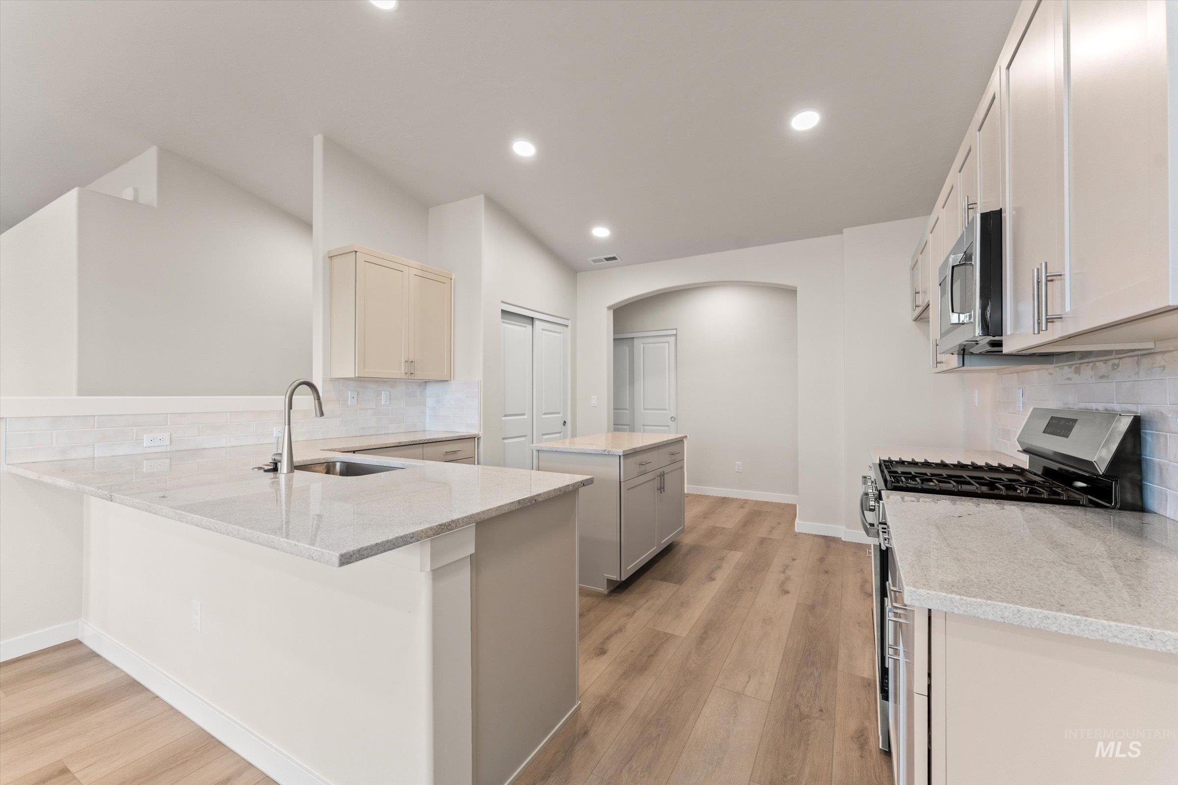 Kitchen with tasteful backsplash, a center island, stainless steel appliances, a peninsula, and light wood-type flooring
