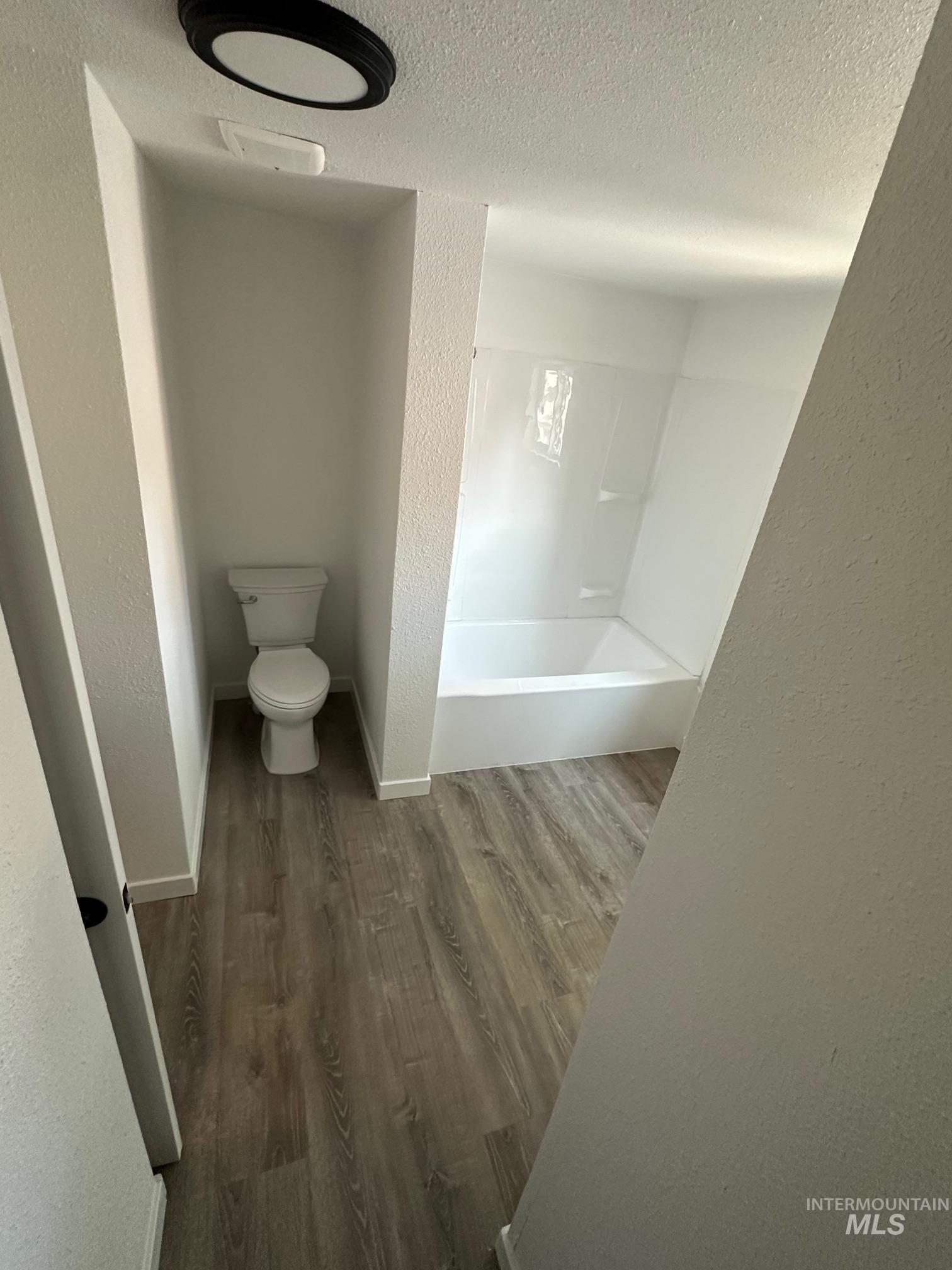 Bathroom with a textured wall, wood finished floors, a textured ceiling, and tub / shower combination