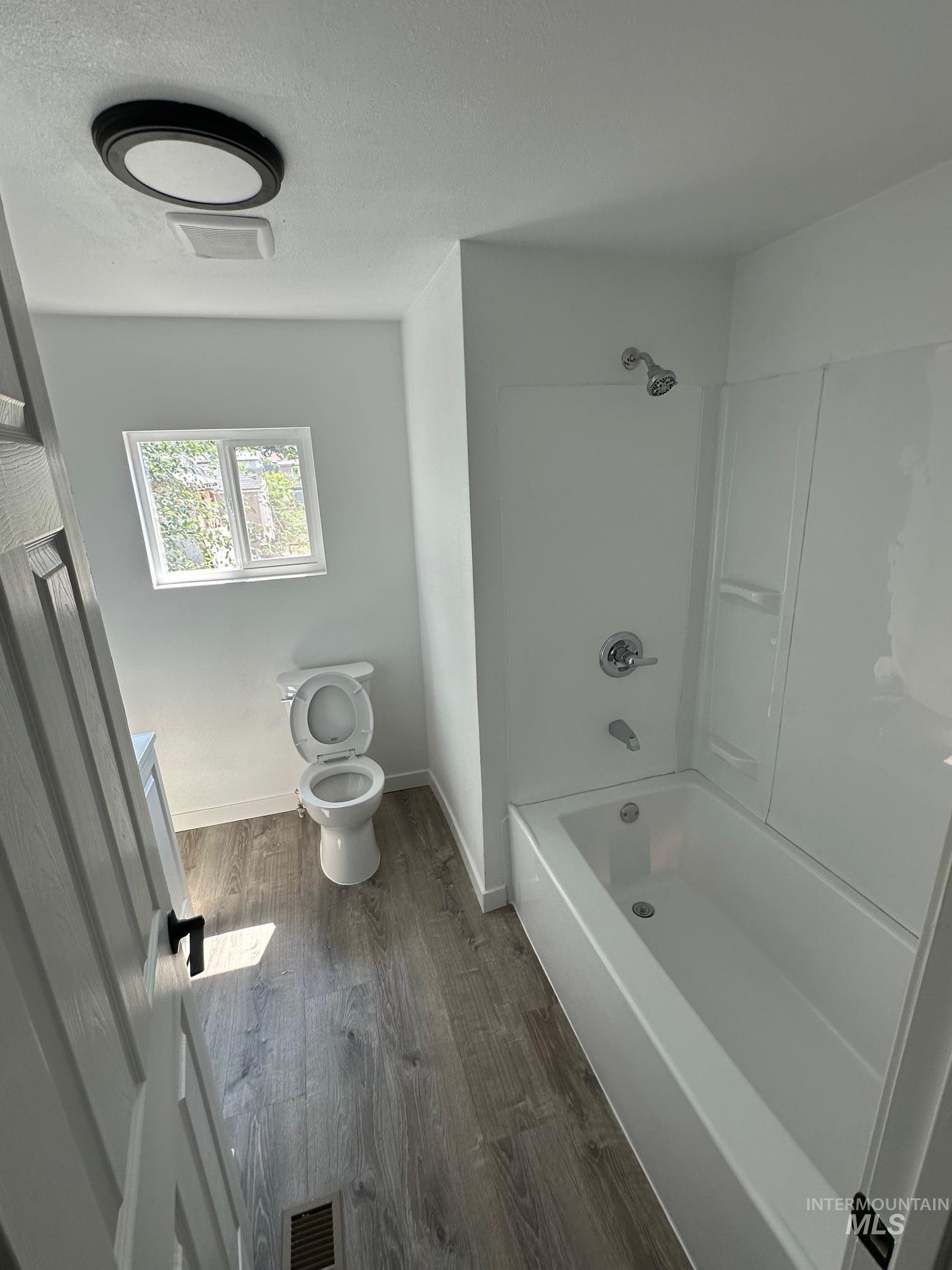 Bathroom with tub / shower combination, dark wood-type flooring, and a textured ceiling