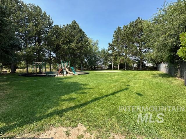 View of green lawn with a playground and view of wooded area