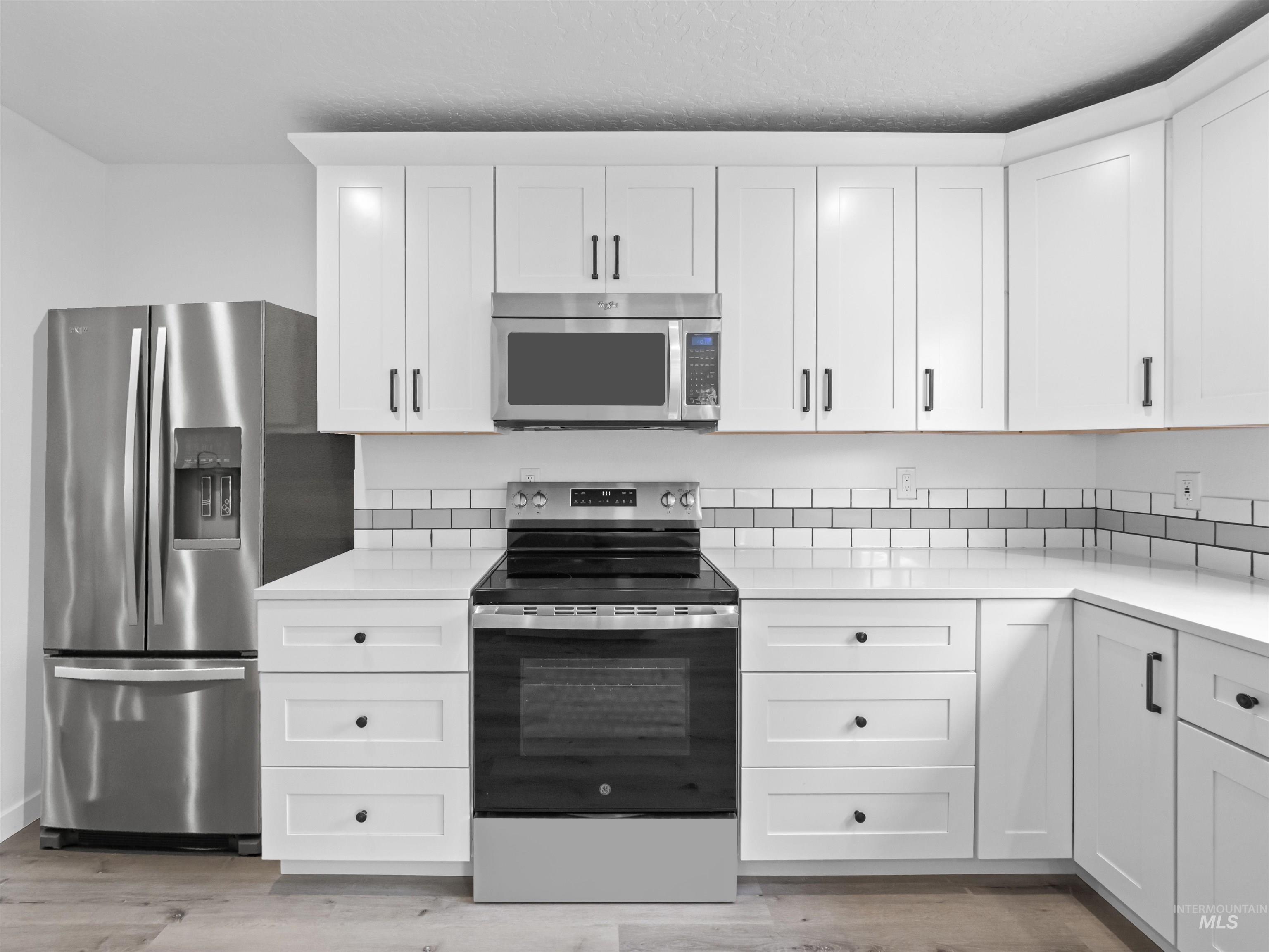 Kitchen with appliances with stainless steel finishes, white cabinets, and light stone countertops