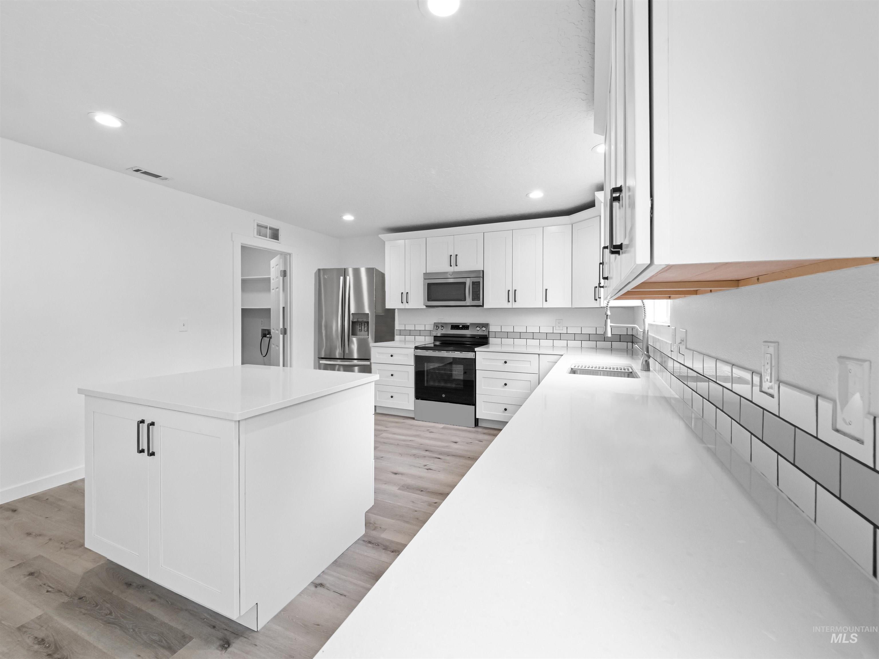 Kitchen featuring white cabinets, stainless steel appliances, light wood-style floors, recessed lighting, and light stone counters