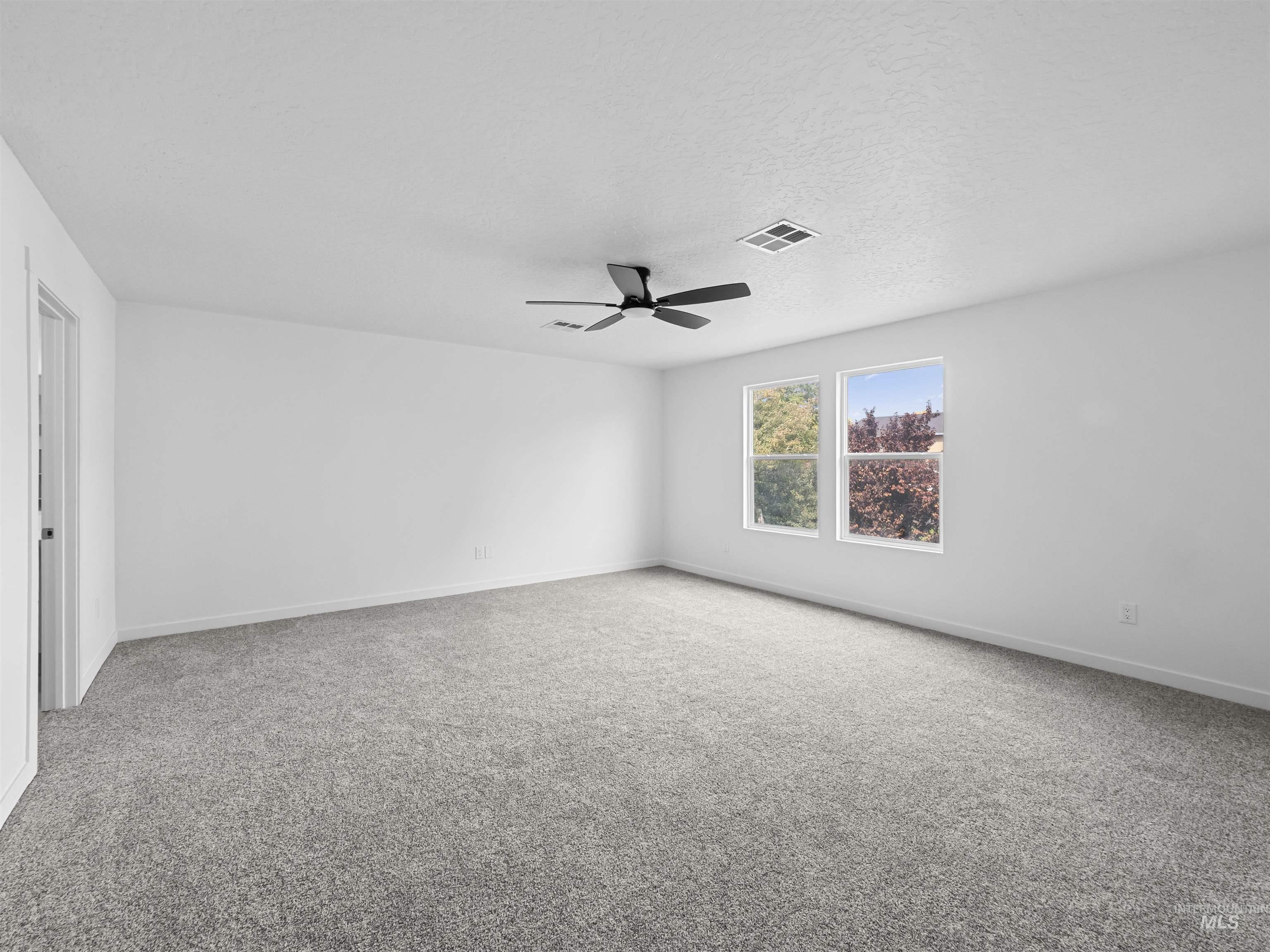 Empty room with light carpet, a ceiling fan, and a textured ceiling