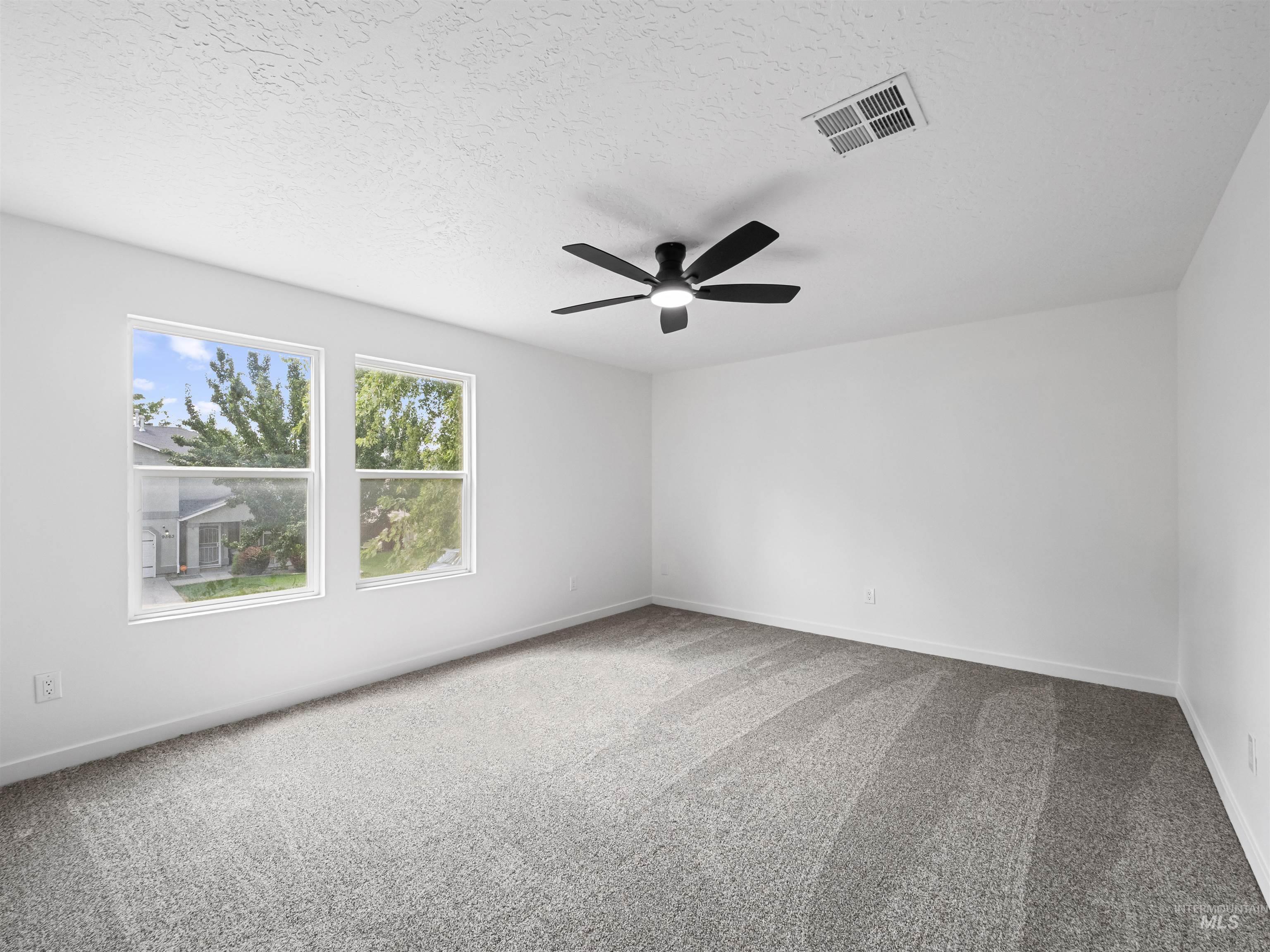 Empty room featuring light colored carpet, a textured ceiling, and a ceiling fan