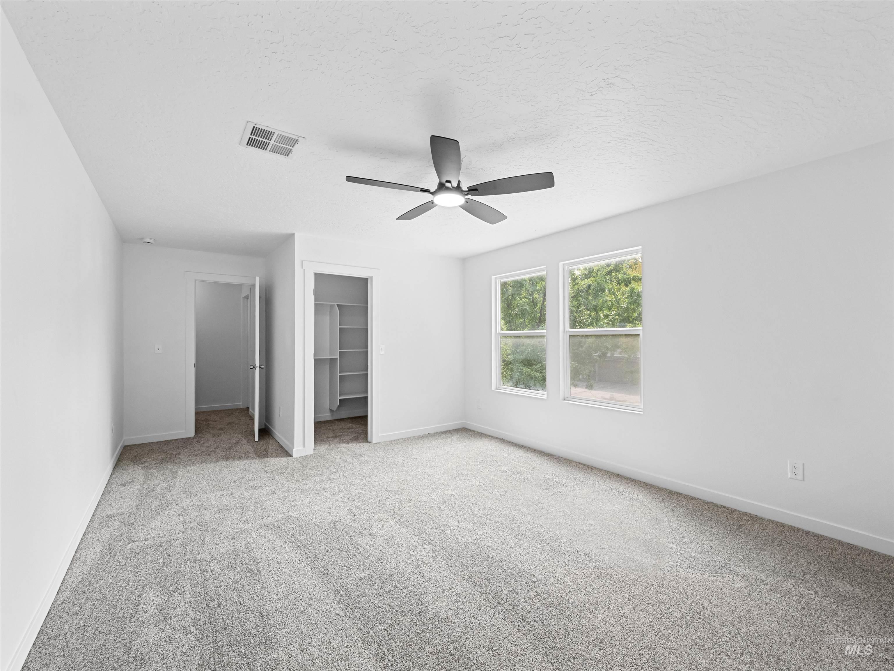 Unfurnished bedroom with a walk in closet, light carpet, ceiling fan, and a textured ceiling