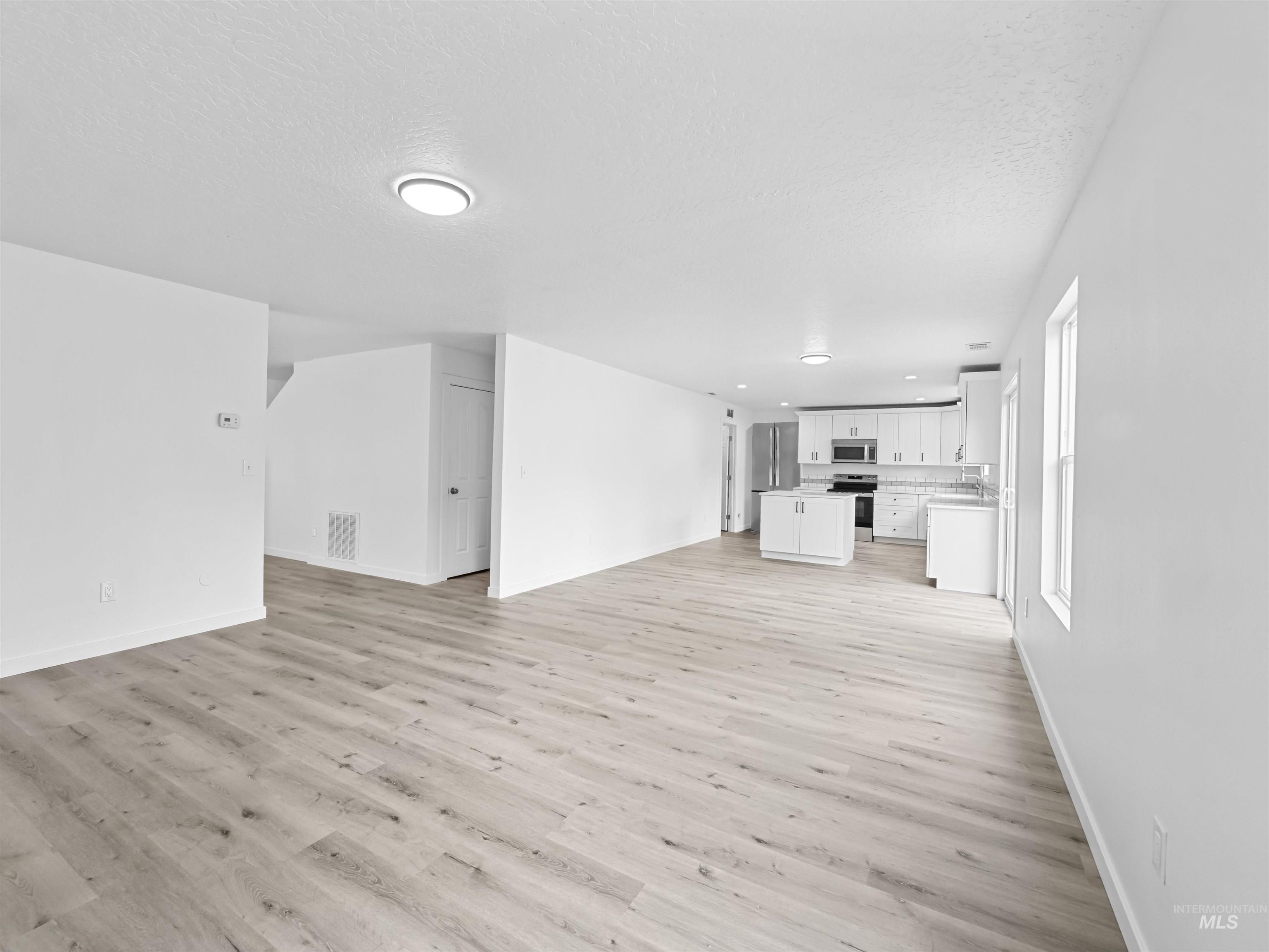 Unfurnished living room featuring light wood-type flooring and a textured ceiling