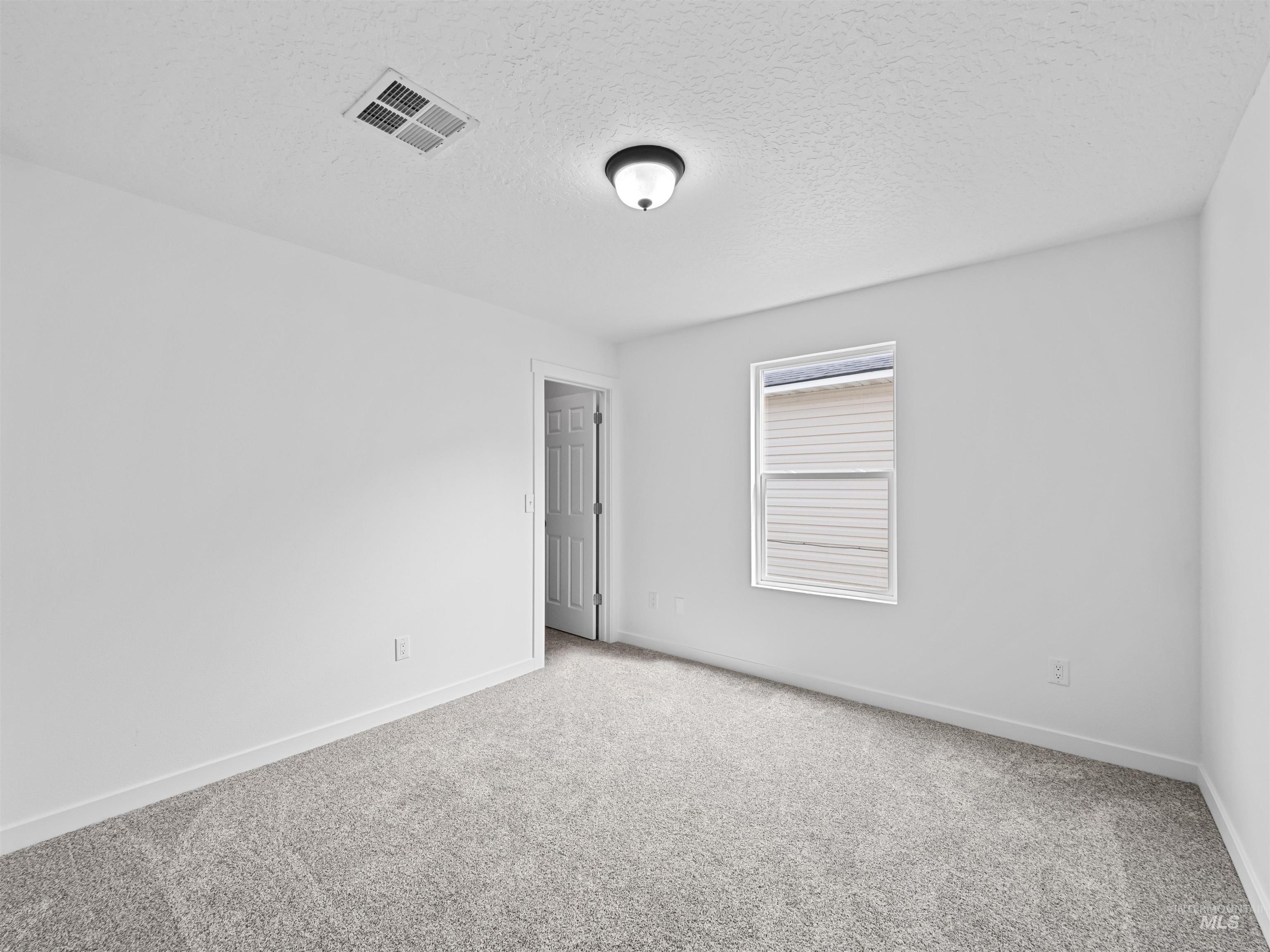 Carpeted empty room with a textured ceiling and baseboards