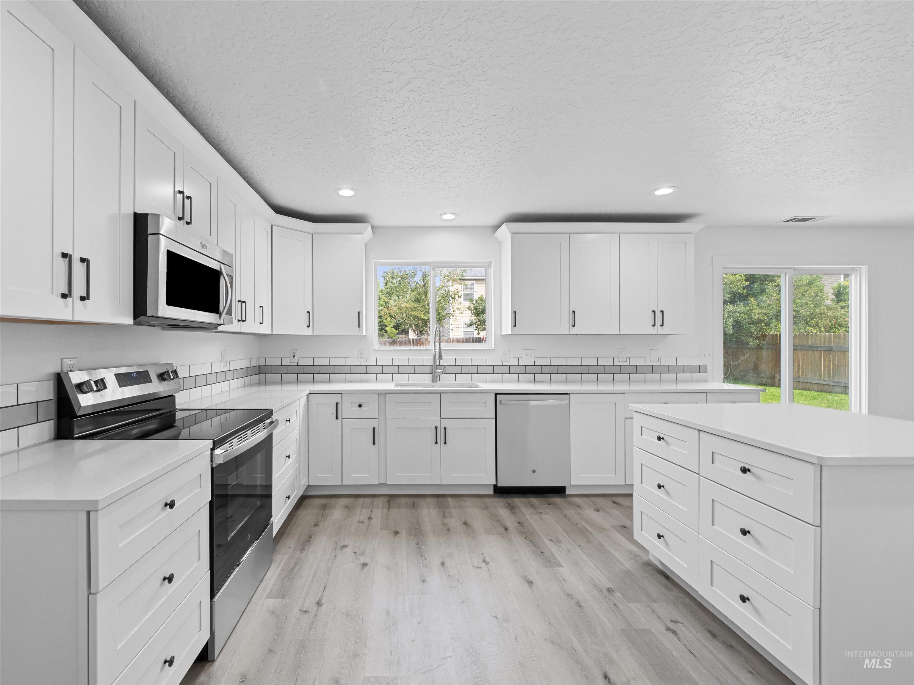 Kitchen with stainless steel appliances, light wood-type flooring, white cabinetry, a textured ceiling, and recessed lighting
