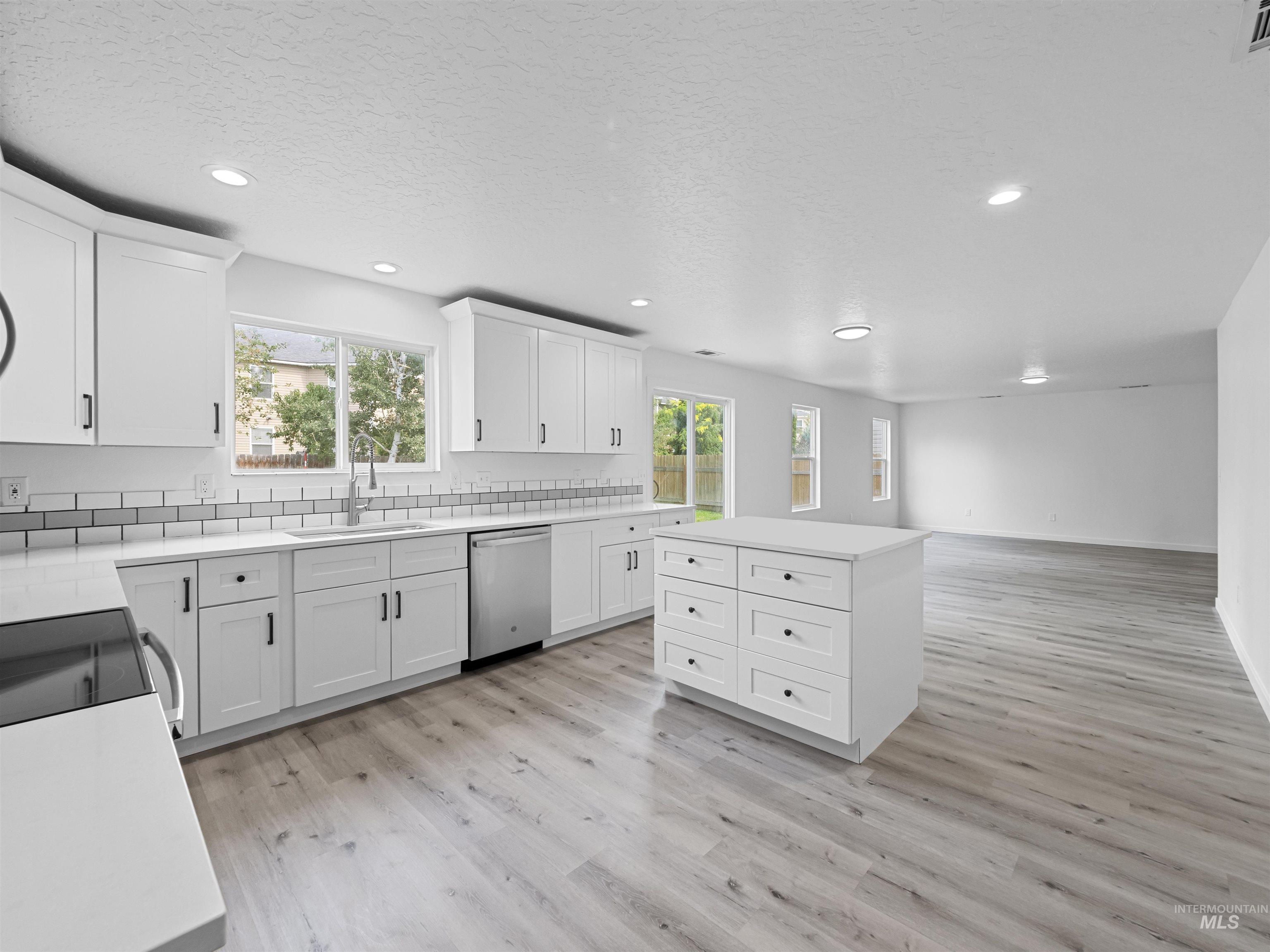 Kitchen with white cabinets, a center island, light wood-style flooring, backsplash, and stainless steel dishwasher