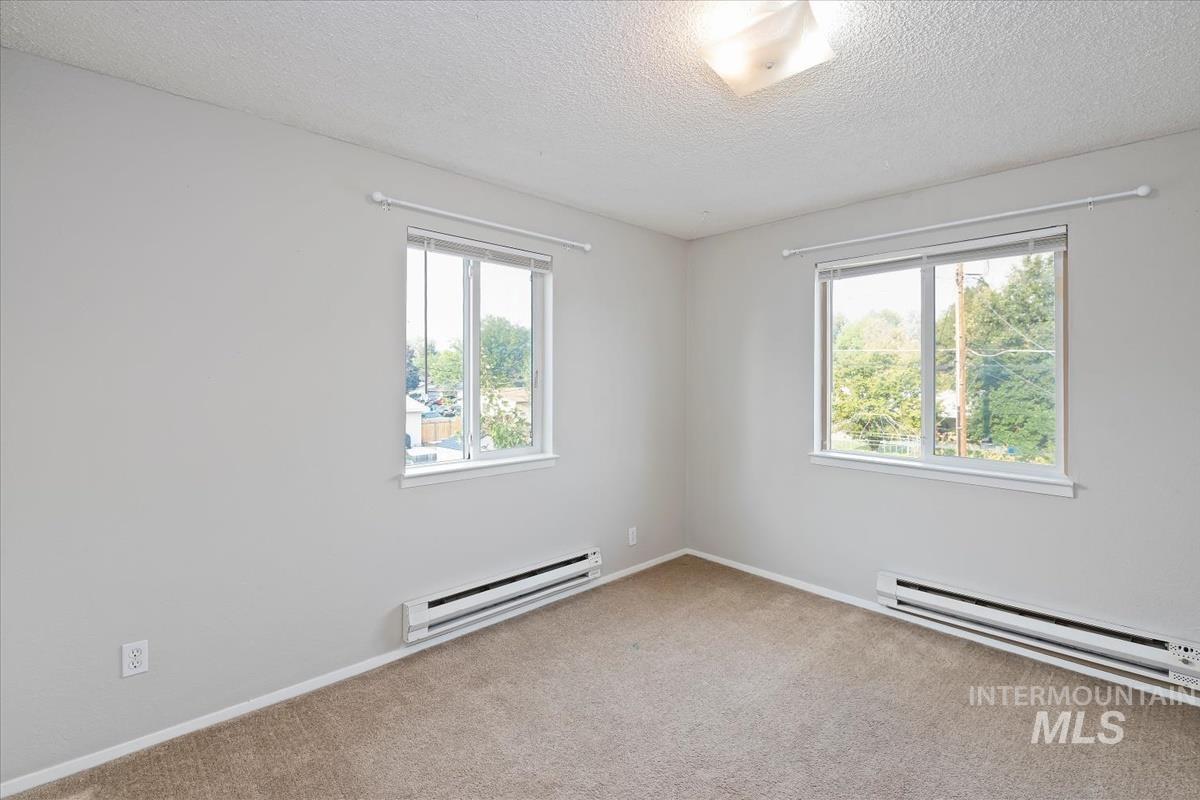 Carpeted empty room featuring baseboard heating and a textured ceiling