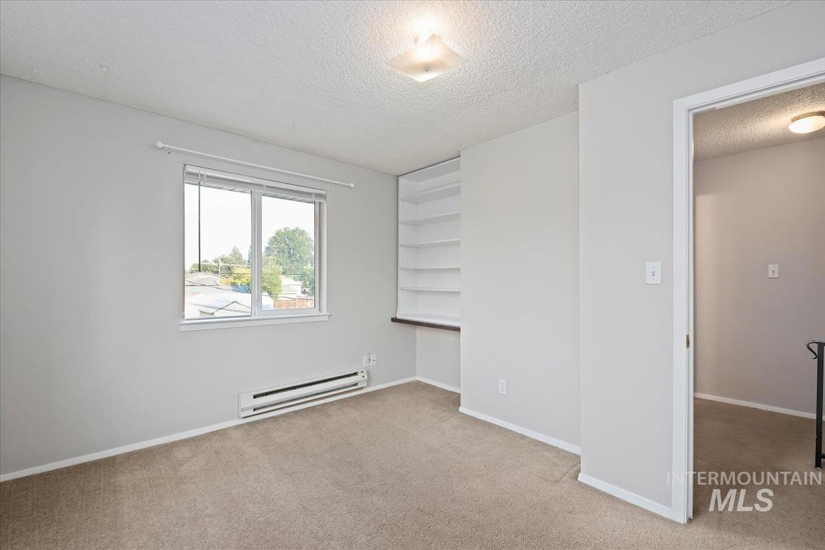 Unfurnished bedroom with a textured ceiling, baseboard heating, and light colored carpet
