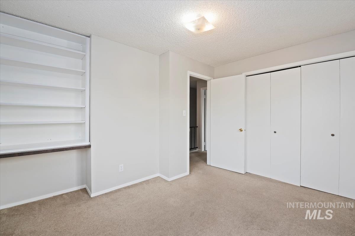 Unfurnished bedroom featuring a textured ceiling, light colored carpet, and a closet