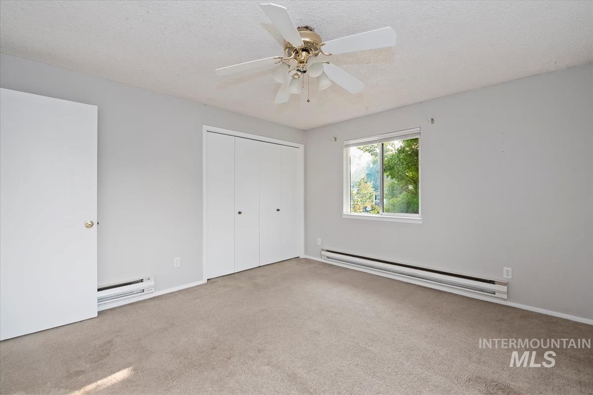Unfurnished bedroom with a baseboard radiator, light colored carpet, a closet, a textured ceiling, and a ceiling fan