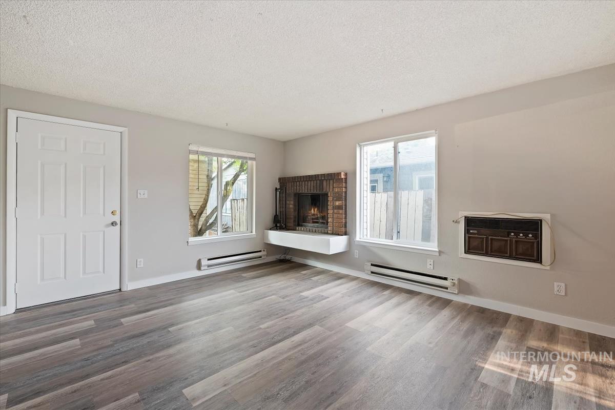 Unfurnished living room featuring a textured ceiling, a baseboard heating unit, healthy amount of natural light, and wood finished floors