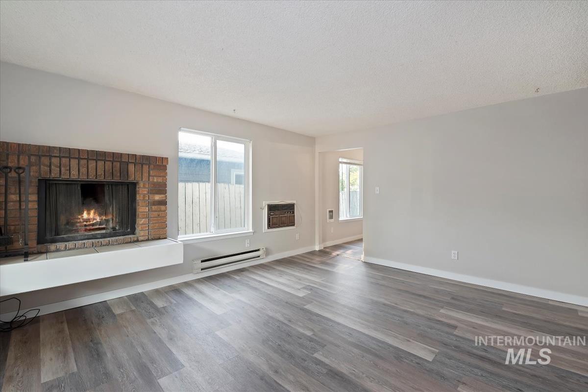 Unfurnished living room with a brick fireplace, wood finished floors, a baseboard heating unit, and a textured ceiling