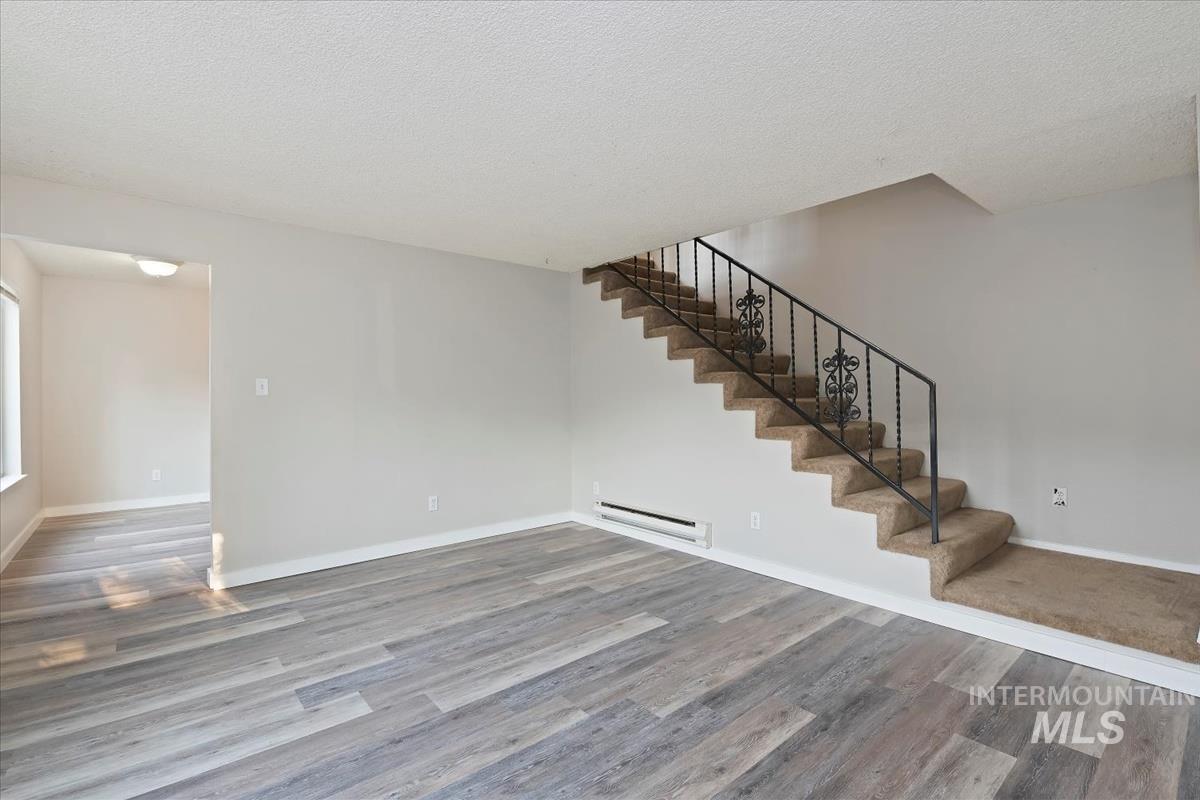 Unfurnished living room featuring a textured ceiling, a baseboard heating unit, light wood-style flooring, and stairway