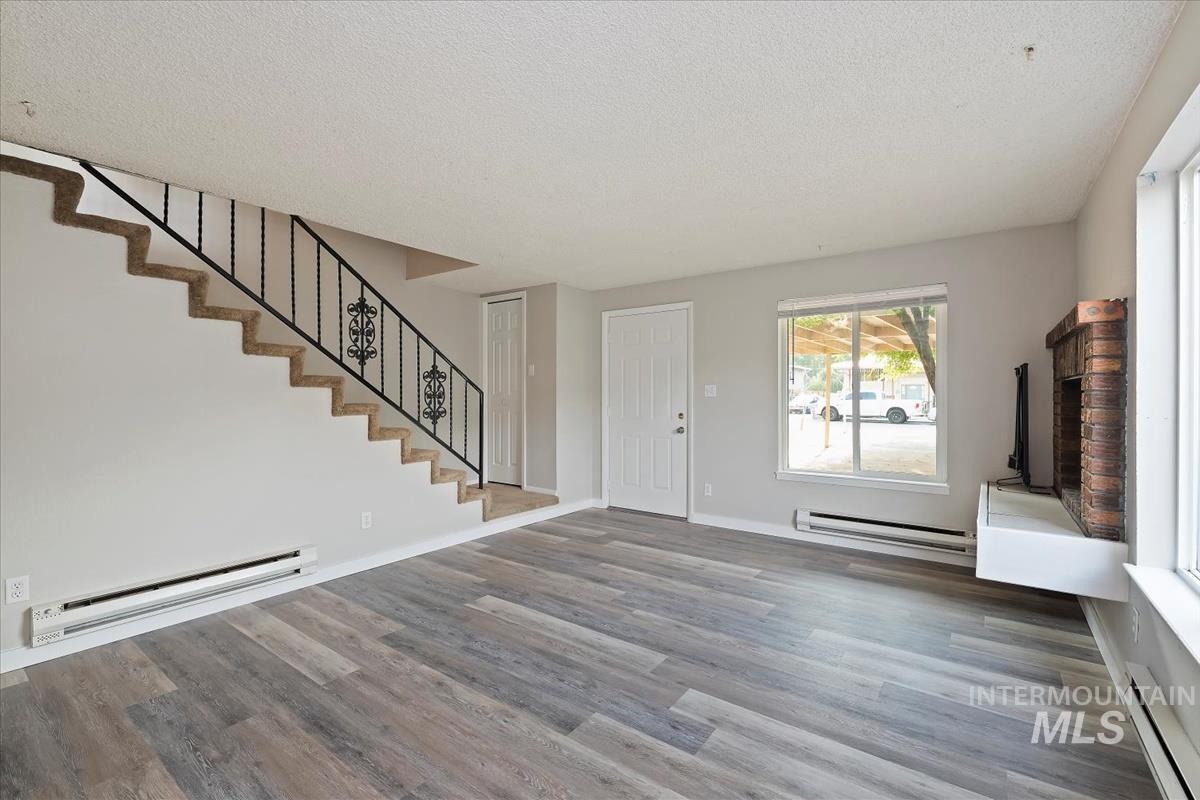Unfurnished living room with a baseboard heating unit, stairs, a textured ceiling, and wood finished floors
