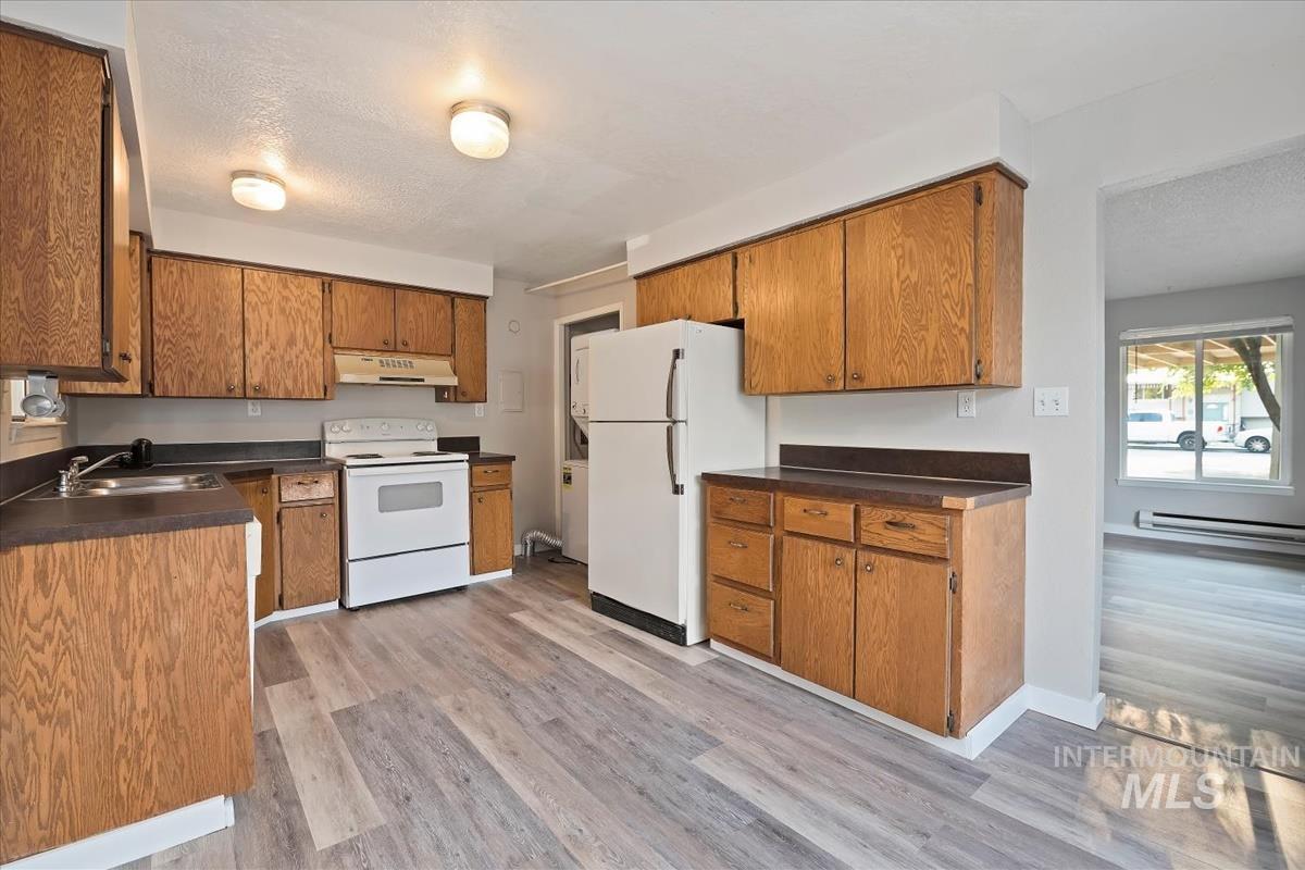 Kitchen featuring white appliances, dark countertops, light wood-style flooring, brown cabinets, and a textured ceiling