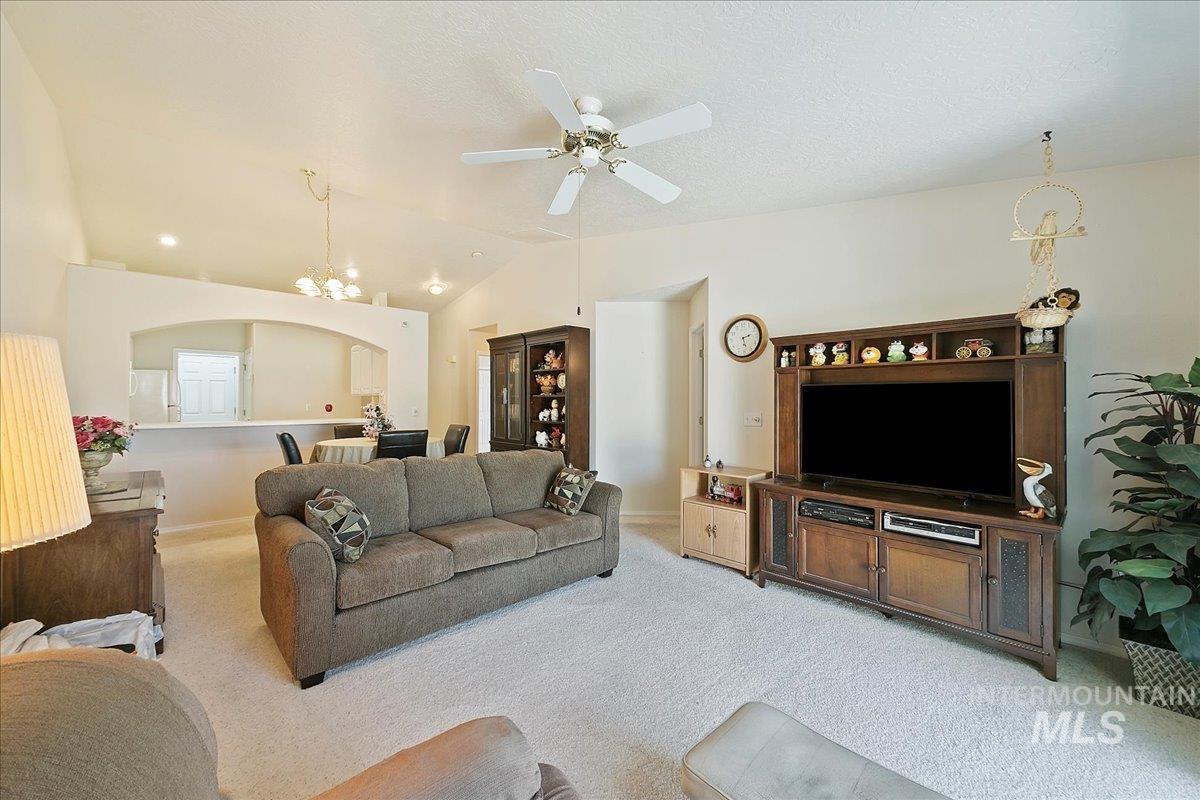Living room with vaulted ceiling, carpet floors, a chandelier, ceiling fan, and a textured ceiling
