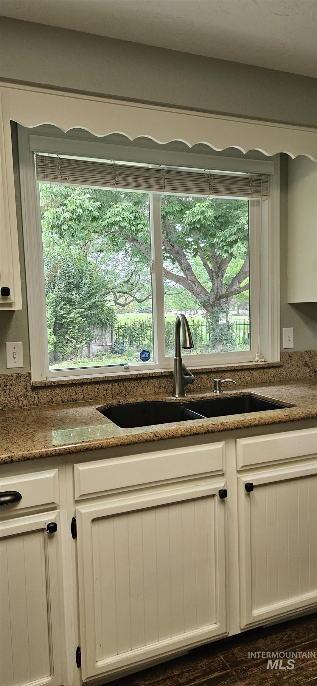 Touch of sophistication black kitchen sink accenting white cabinets and wood tiled flooring.  Lots of sunlight with view of parklike yard setting and golf course.