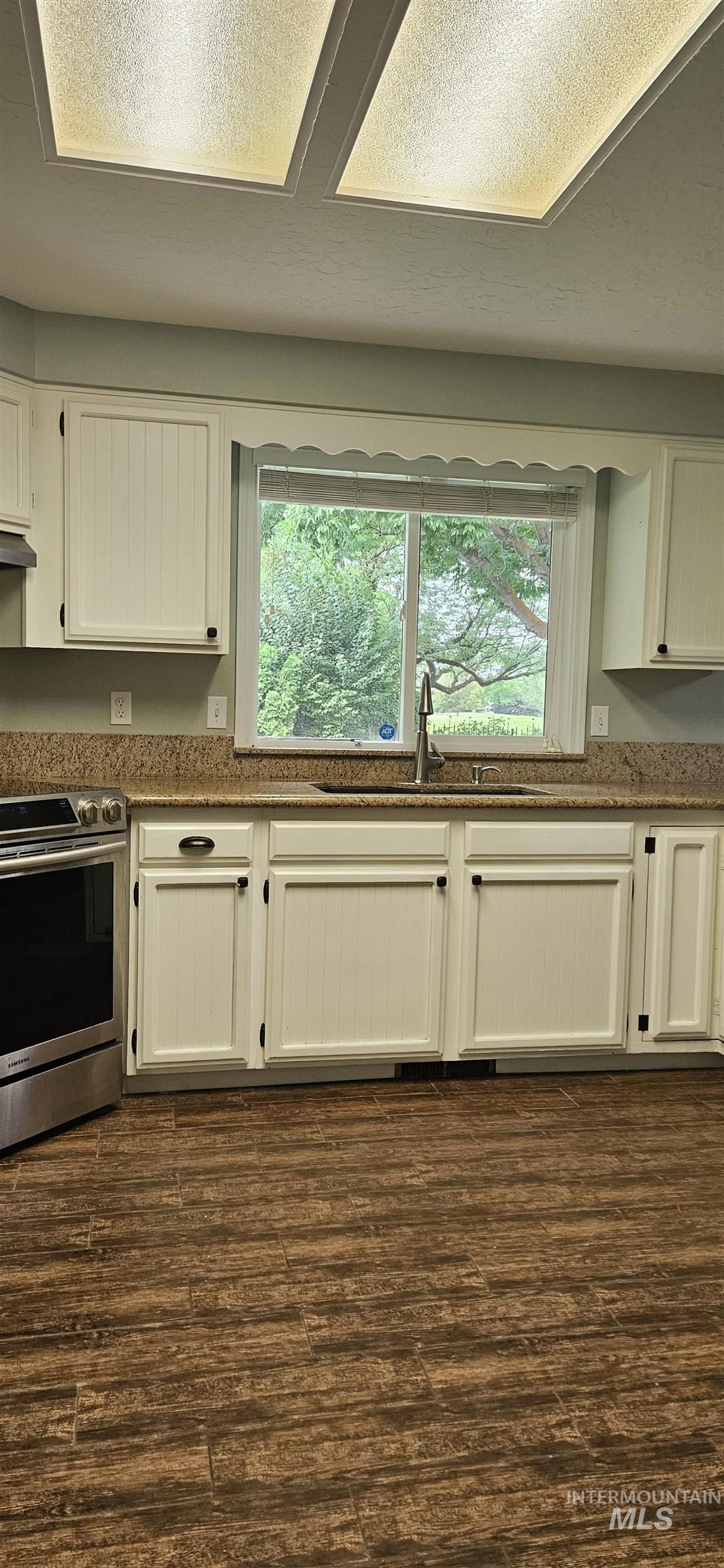Kitchen featuring stainless steel electric range and fan, white cabinetry, plenty of natural light, and dark wood-style floors. Enjoy the golf course view!