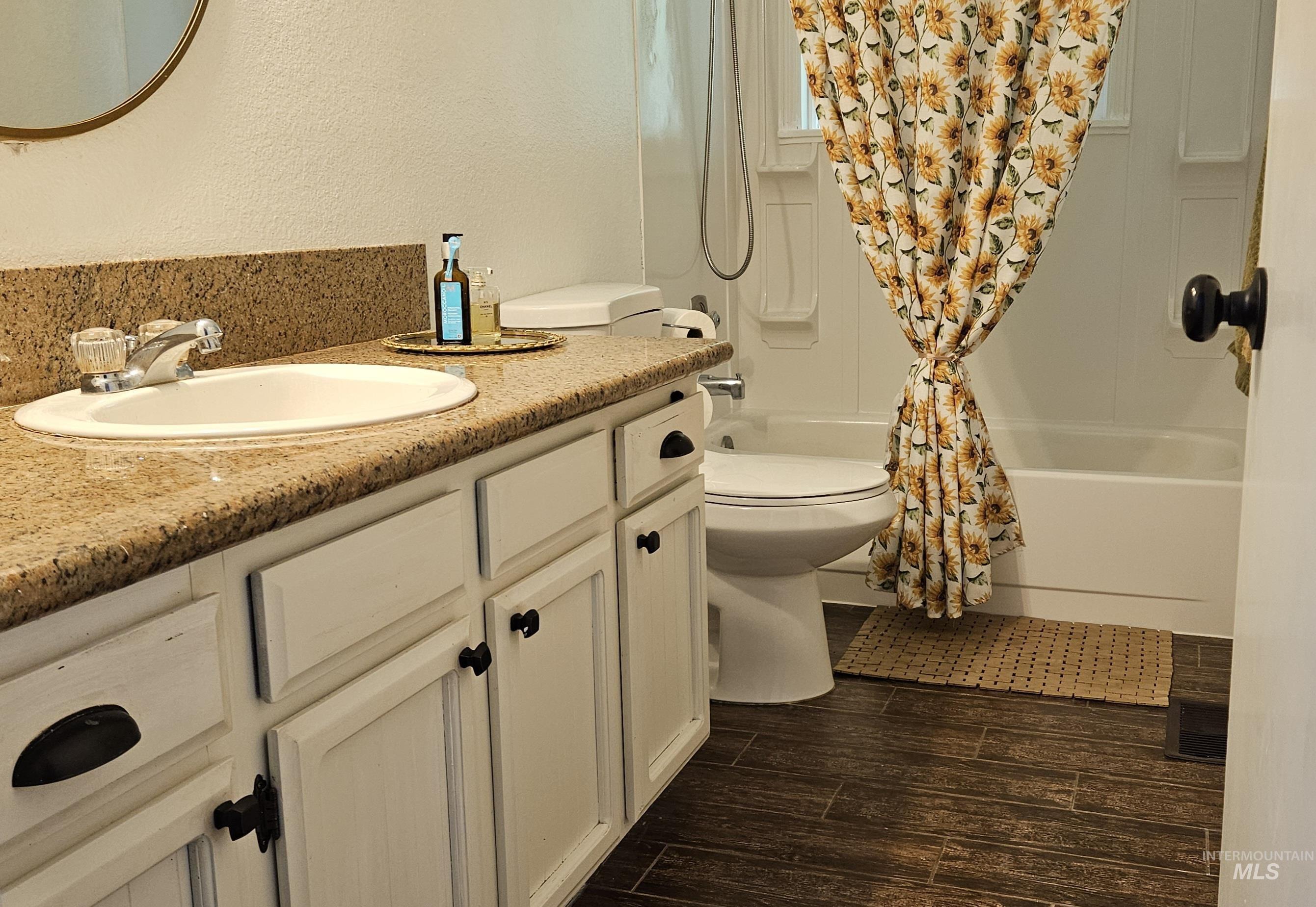 Full bathroom with shower / bathtub combination with curtain, vanity, circular mirror, wood finished floors, window, 