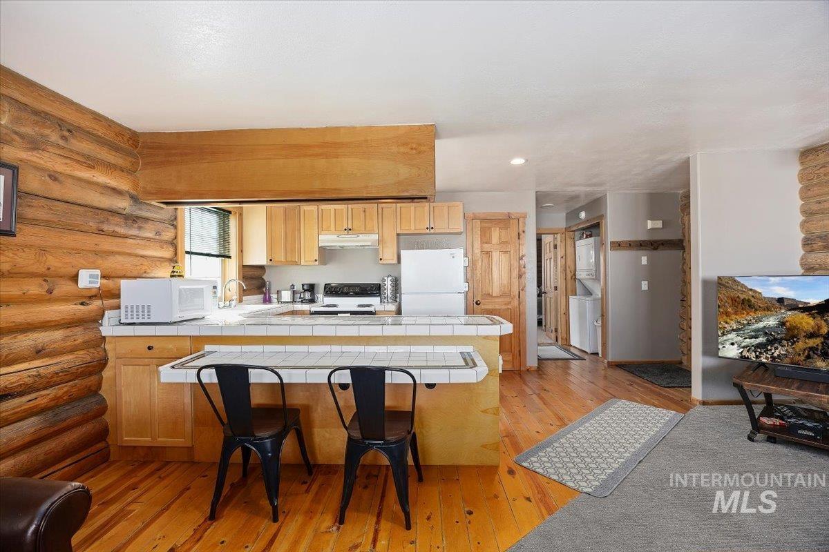 Kitchen with light wood-style floors, white appliances, a peninsula, light brown cabinetry, and tile counters