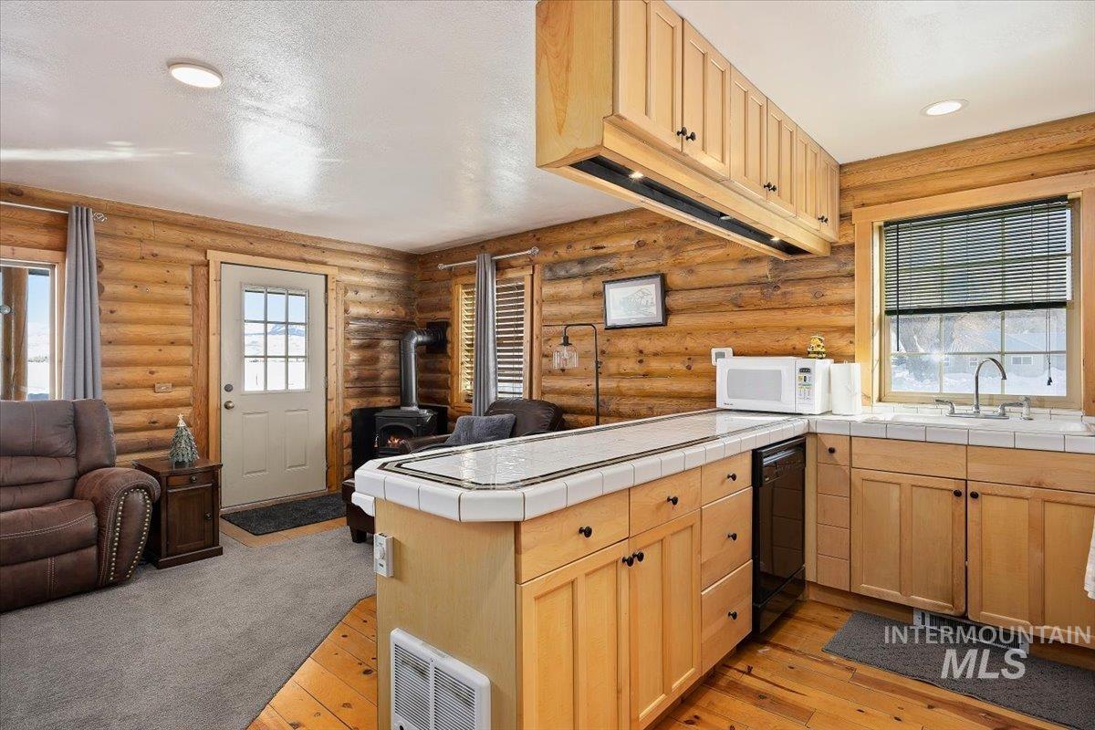 Kitchen featuring light brown cabinetry, open floor plan, a wood stove, a peninsula, and log walls
