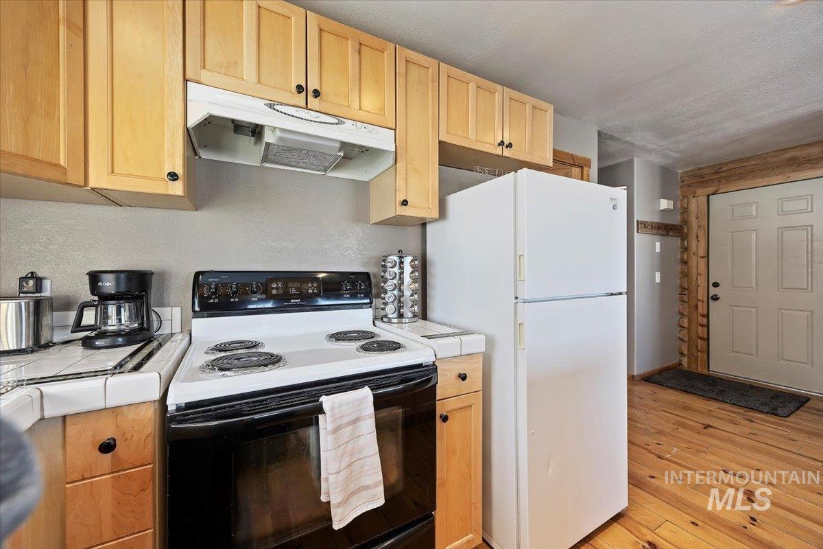 Kitchen featuring tile countertops, electric stove, under cabinet range hood, freestanding refrigerator, and light brown cabinets