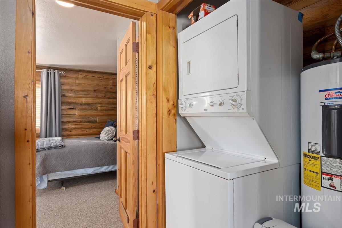 Laundry area with electric water heater, log walls, carpet, and stacked washer / dryer