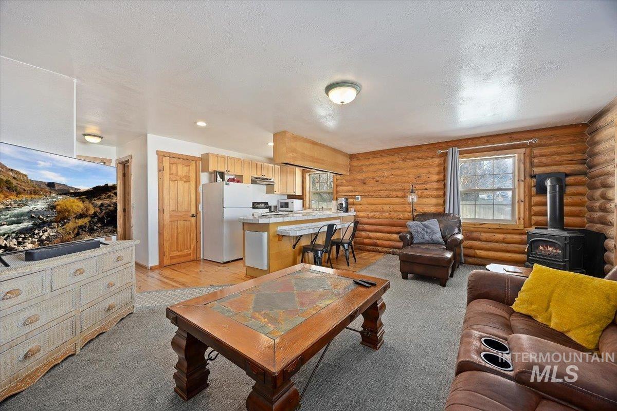 Living room with a wood stove, a textured ceiling, log walls, and light wood-style floors