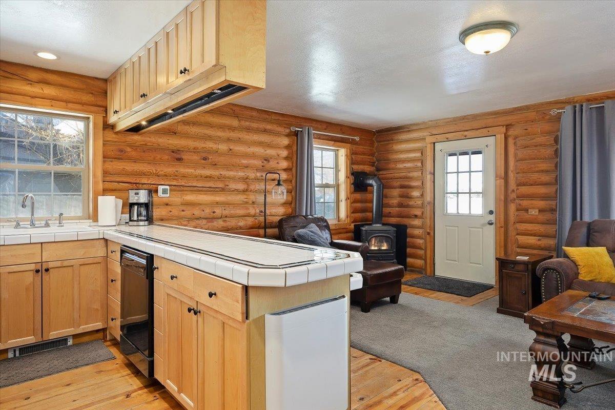 Kitchen featuring light wood-style floors, tile countertops, a wood stove, log walls, and dishwasher
