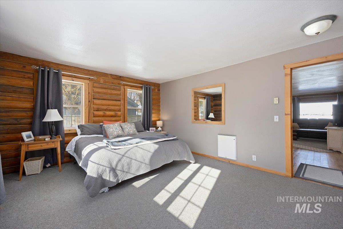Bedroom featuring multiple windows, carpet flooring, and rustic walls