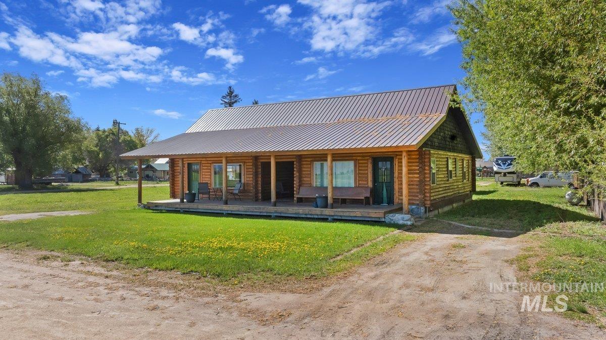 Rear view of house featuring a porch, a yard, a metal roof, and log siding